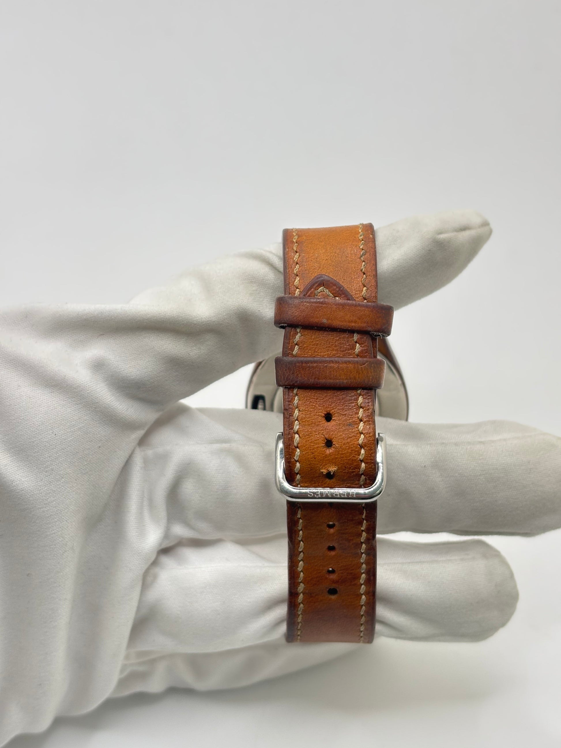 Montre Hermès Harnais HA3.410 en acier avec mouvement quartz, cadran blanc et bracelet en cuir brun. Modèle homme et unisexe au design élégant avec verre saphir et fonction date. Montre d’occasion en très bon état avec légères traces d’usure et micro-rayures discrètes. Format 30 mm idéal pour un style classique et raffiné.