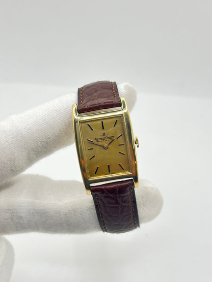 Montre Jaeger-LeCoultre Classic 9012 vintage à remontage manuel, datant approximativement de 1960. Son boîtier rectangulaire en or jaune de 37 × 23 mm est équipé d’un verre Plexiglas et d’un élégant cadran or à index bâtons. Cette montre Jaeger-LeCoultre est montée sur un bracelet brun en cuir de crocodile avec boucle ardillon en acier. En très bon état, elle présente de légères traces d’usure et est proposée avec son coffret d’origine.
