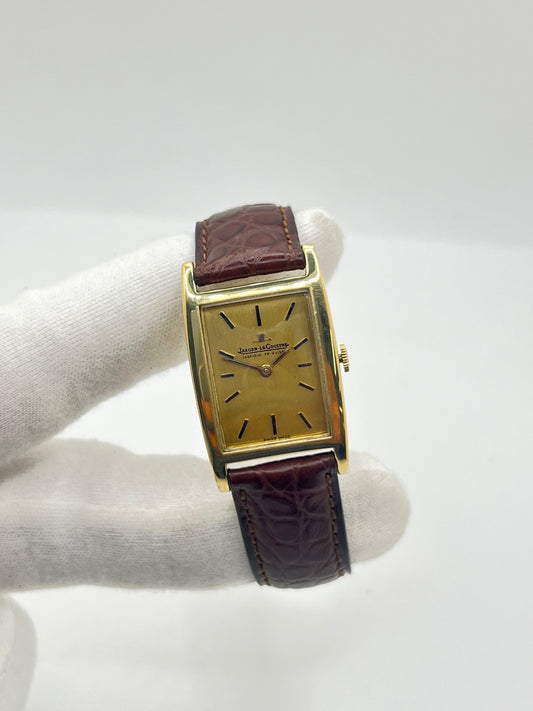 Montre Jaeger-LeCoultre Classic 9012 vintage à remontage manuel, datant approximativement de 1960. Son boîtier rectangulaire en or jaune de 37 × 23 mm est équipé d’un verre Plexiglas et d’un élégant cadran or à index bâtons. Cette montre Jaeger-LeCoultre est montée sur un bracelet brun en cuir de crocodile avec boucle ardillon en acier. En très bon état, elle présente de légères traces d’usure et est proposée avec son coffret d’origine.