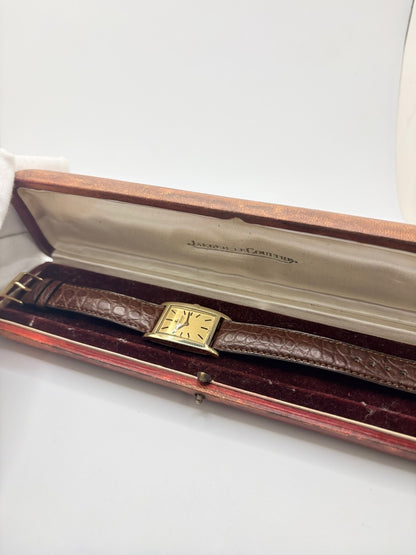 Montre Jaeger-LeCoultre Classic 9012 vintage à remontage manuel, datant approximativement de 1960. Son boîtier rectangulaire en or jaune de 37 × 23 mm est équipé d’un verre Plexiglas et d’un élégant cadran or à index bâtons. Cette montre Jaeger-LeCoultre est montée sur un bracelet brun en cuir de crocodile avec boucle ardillon en acier. En très bon état, elle présente de légères traces d’usure et est proposée avec son coffret d’origine.
