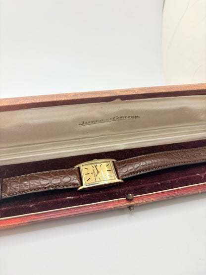 Montre Jaeger-LeCoultre Classic 9012 vintage à remontage manuel, datant approximativement de 1960. Son boîtier rectangulaire en or jaune de 37 × 23 mm est équipé d’un verre Plexiglas et d’un élégant cadran or à index bâtons. Cette montre Jaeger-LeCoultre est montée sur un bracelet brun en cuir de crocodile avec boucle ardillon en acier. En très bon état, elle présente de légères traces d’usure et est proposée avec son coffret d’origine.