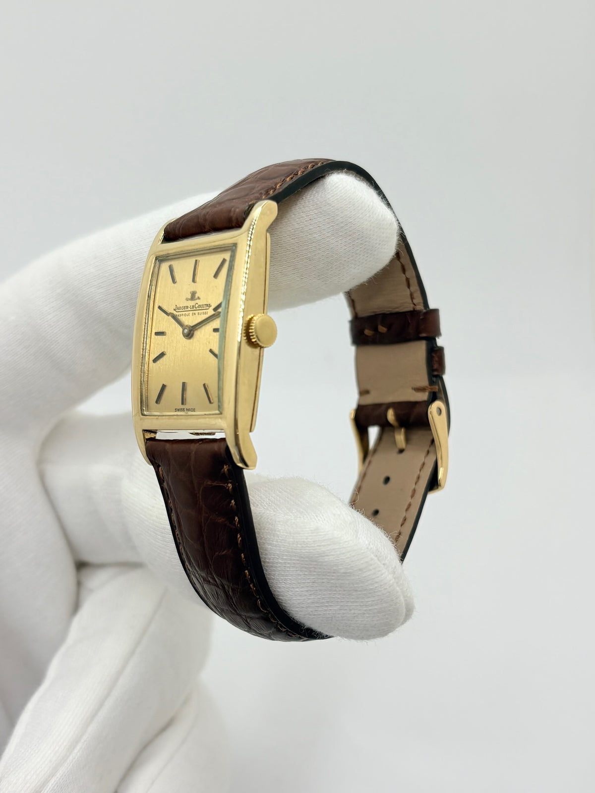 Montre Jaeger-LeCoultre Classic 9012 vintage à remontage manuel, datant approximativement de 1960. Son boîtier rectangulaire en or jaune de 37 × 23 mm est équipé d’un verre Plexiglas et d’un élégant cadran or à index bâtons. Cette montre Jaeger-LeCoultre est montée sur un bracelet brun en cuir de crocodile avec boucle ardillon en acier. En très bon état, elle présente de légères traces d’usure et est proposée avec son coffret d’origine.