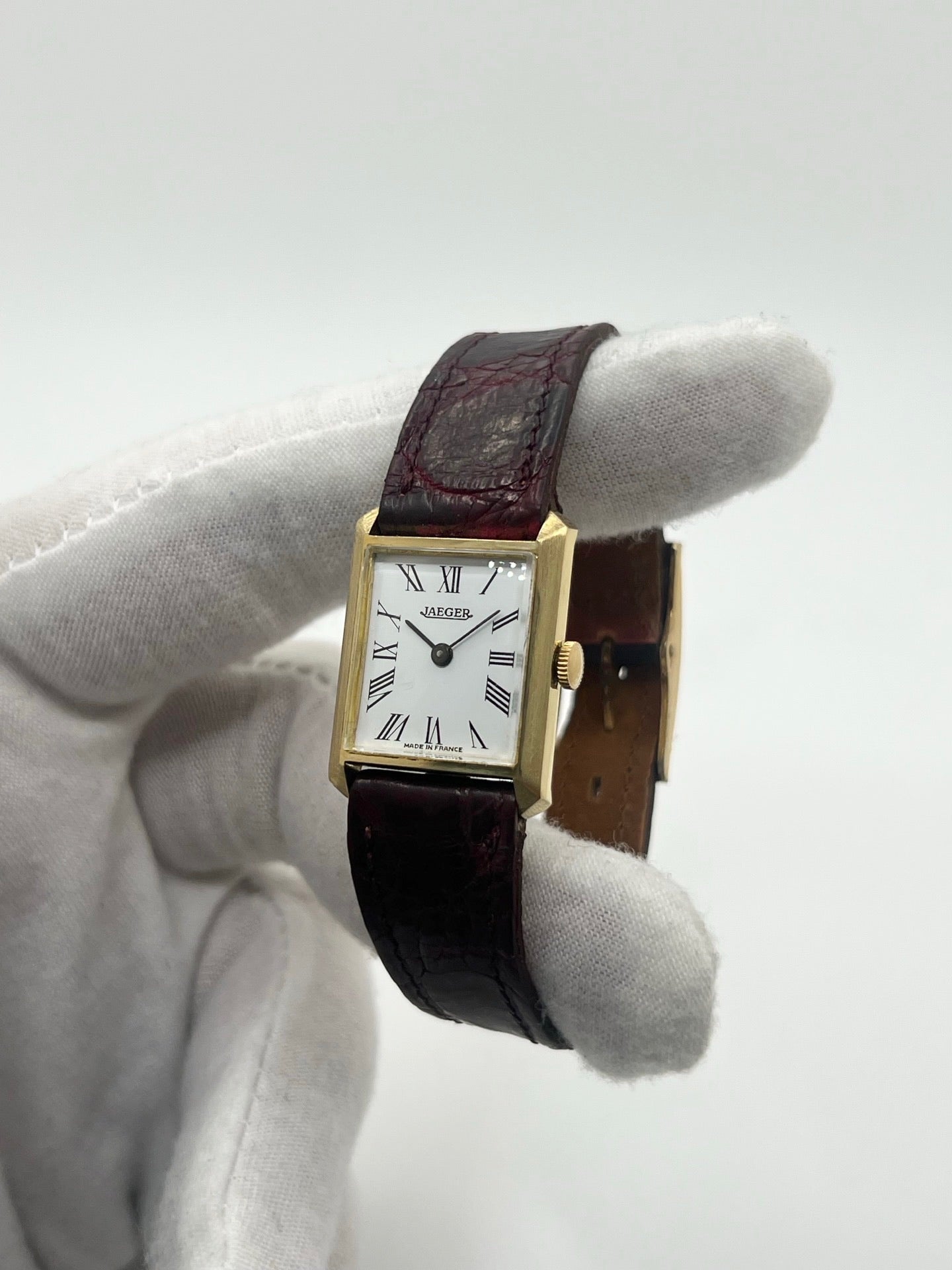 Montre vintage classique en or jaune 18 carats avec boîtier rond de 20 mm, mouvement mécanique à remontage manuel et cadran blanc à chiffres romains. Montre élégante au style intemporel, dotée d’un verre minéral et d’un bracelet en cuir bordeaux avec boucle déployante en acier. Modèle ancien révisé, en très bon état, idéal pour les amateurs de montres de collection et d’horlogerie traditionnelle.