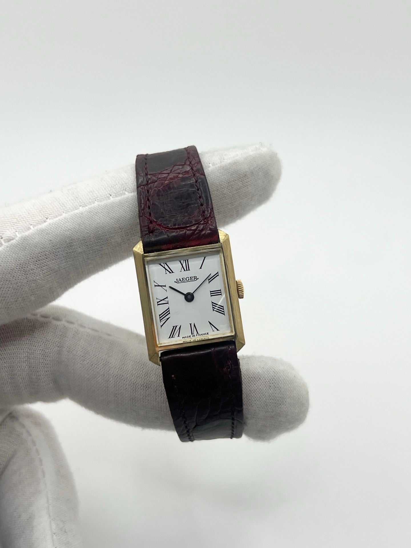 Montre vintage classique en or jaune 18 carats avec boîtier rond de 20 mm, mouvement mécanique à remontage manuel et cadran blanc à chiffres romains. Montre élégante au style intemporel, dotée d’un verre minéral et d’un bracelet en cuir bordeaux avec boucle déployante en acier. Modèle ancien révisé, en très bon état, idéal pour les amateurs de montres de collection et d’horlogerie traditionnelle.