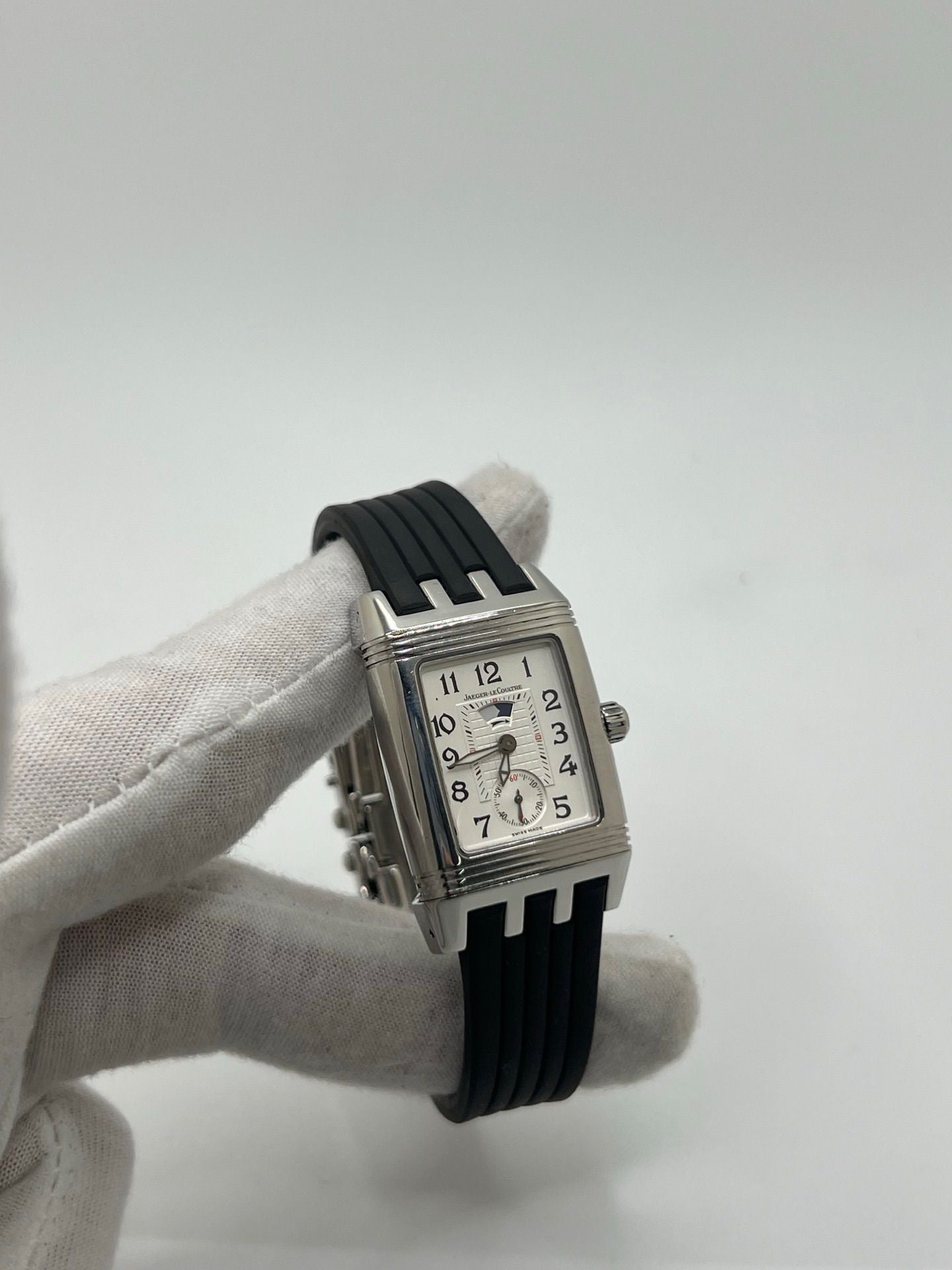 Montre Reverso Duetto référence 296.8.74 en acier, format rectangulaire, équipée d’un mouvement à remontage manuel. Modèle pour femme avec cadran blanc à chiffres arabes et verre saphir. Brace­let en caoutchouc noir avec boucle double plis. Pièce d’occasion en très bon état, présentant de légères traces d’usure discrètes.