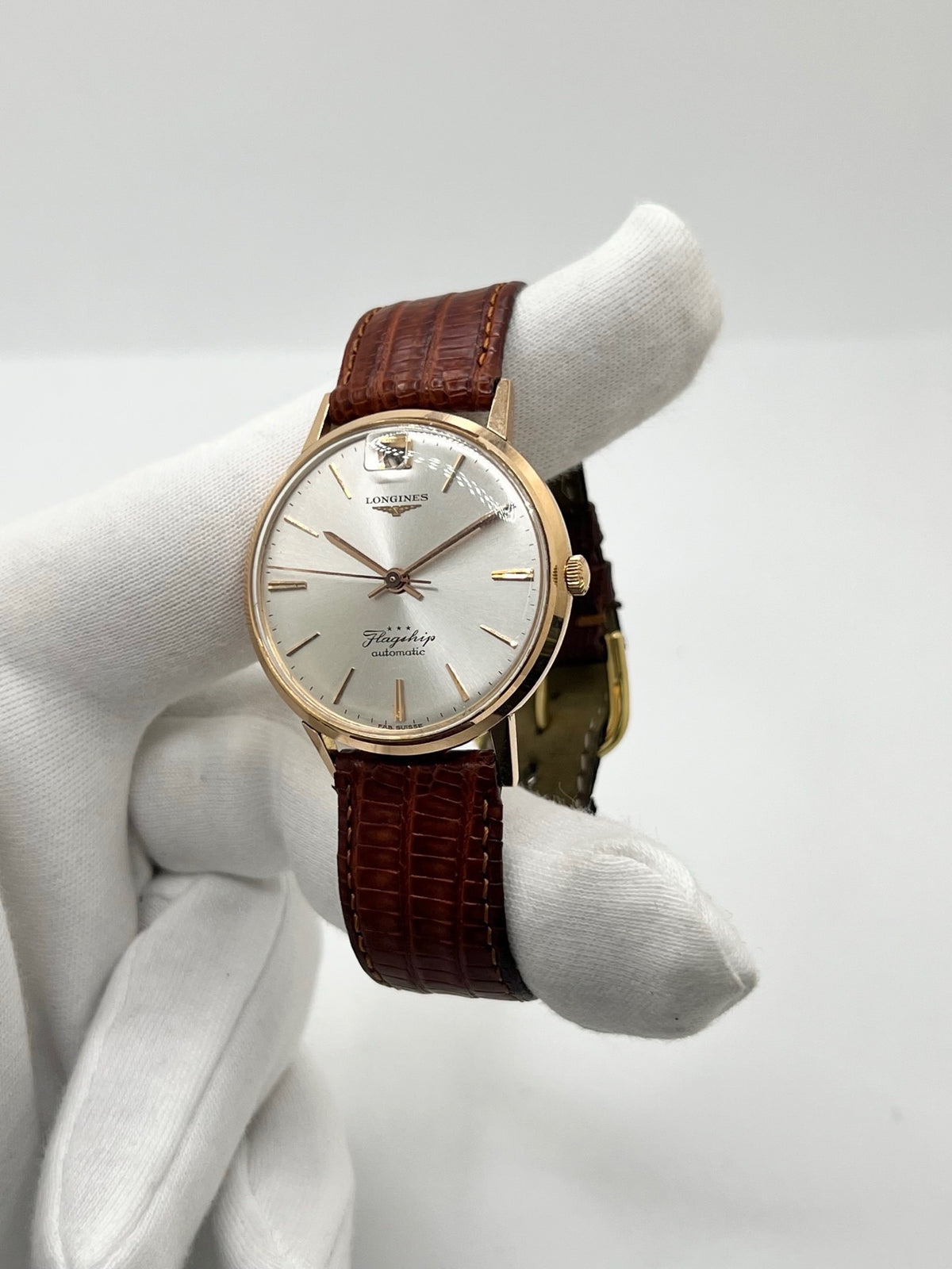 Montre Longines Flagship 2407 vintage en très bon état, datant approximativement de 1962, avec mouvement automatique calibre 341. Son boîtier de 35 mm en or rose est associé à un cadran argent à index bâtons et un verre Plexiglas. Cette Longines Flagship possède un bracelet en cuir de lézard brun avec boucle ardillon en acier. Elle dispose également d’une fonction date et d’un design élégant et intemporel.
