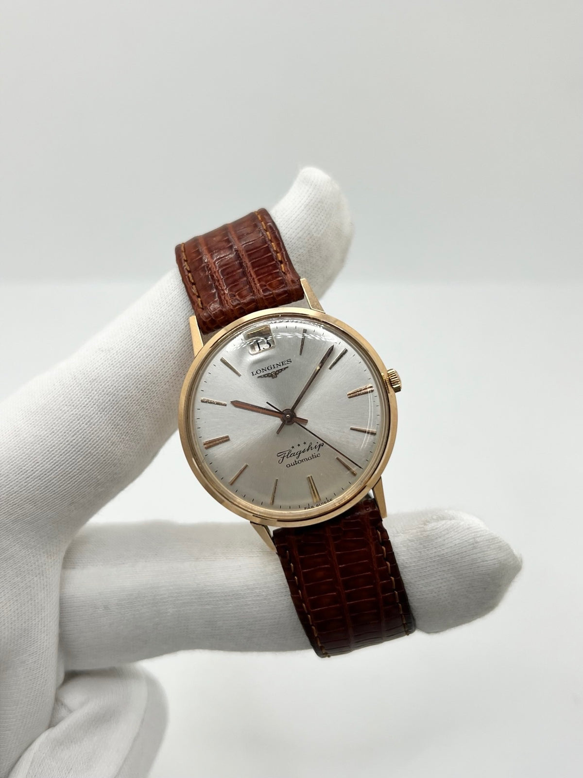 Montre Longines Flagship 2407 vintage en très bon état, datant approximativement de 1962, avec mouvement automatique calibre 341. Son boîtier de 35 mm en or rose est associé à un cadran argent à index bâtons et un verre Plexiglas. Cette Longines Flagship possède un bracelet en cuir de lézard brun avec boucle ardillon en acier. Elle dispose également d’une fonction date et d’un design élégant et intemporel.