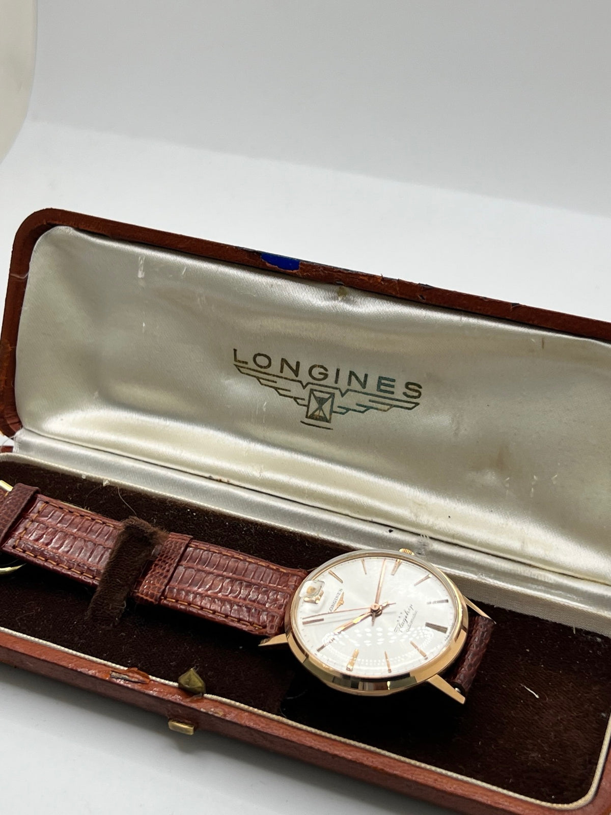 Montre Longines Flagship 2407 vintage en très bon état, datant approximativement de 1962, avec mouvement automatique calibre 341. Son boîtier de 35 mm en or rose est associé à un cadran argent à index bâtons et un verre Plexiglas. Cette Longines Flagship possède un bracelet en cuir de lézard brun avec boucle ardillon en acier. Elle dispose également d’une fonction date et d’un design élégant et intemporel.
