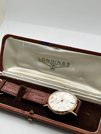 Montre Longines Flagship 2407 vintage en très bon état, datant approximativement de 1962, avec mouvement automatique calibre 341. Son boîtier de 35 mm en or rose est associé à un cadran argent à index bâtons et un verre Plexiglas. Cette Longines Flagship possède un bracelet en cuir de lézard brun avec boucle ardillon en acier. Elle dispose également d’une fonction date et d’un design élégant et intemporel.