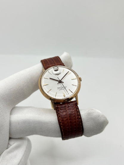 Montre Longines Flagship 2407 vintage en très bon état, datant approximativement de 1962, avec mouvement automatique calibre 341. Son boîtier de 35 mm en or rose est associé à un cadran argent à index bâtons et un verre Plexiglas. Cette Longines Flagship possède un bracelet en cuir de lézard brun avec boucle ardillon en acier. Elle dispose également d’une fonction date et d’un design élégant et intemporel.