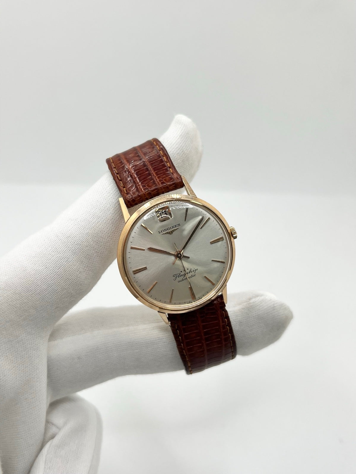 Montre Longines Flagship 2407 vintage en très bon état, datant approximativement de 1962, avec mouvement automatique calibre 341. Son boîtier de 35 mm en or rose est associé à un cadran argent à index bâtons et un verre Plexiglas. Cette Longines Flagship possède un bracelet en cuir de lézard brun avec boucle ardillon en acier. Elle dispose également d’une fonction date et d’un design élégant et intemporel.