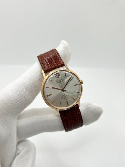 Montre Longines Flagship 2407 vintage en très bon état, datant approximativement de 1962, avec mouvement automatique calibre 341. Son boîtier de 35 mm en or rose est associé à un cadran argent à index bâtons et un verre Plexiglas. Cette Longines Flagship possède un bracelet en cuir de lézard brun avec boucle ardillon en acier. Elle dispose également d’une fonction date et d’un design élégant et intemporel.
