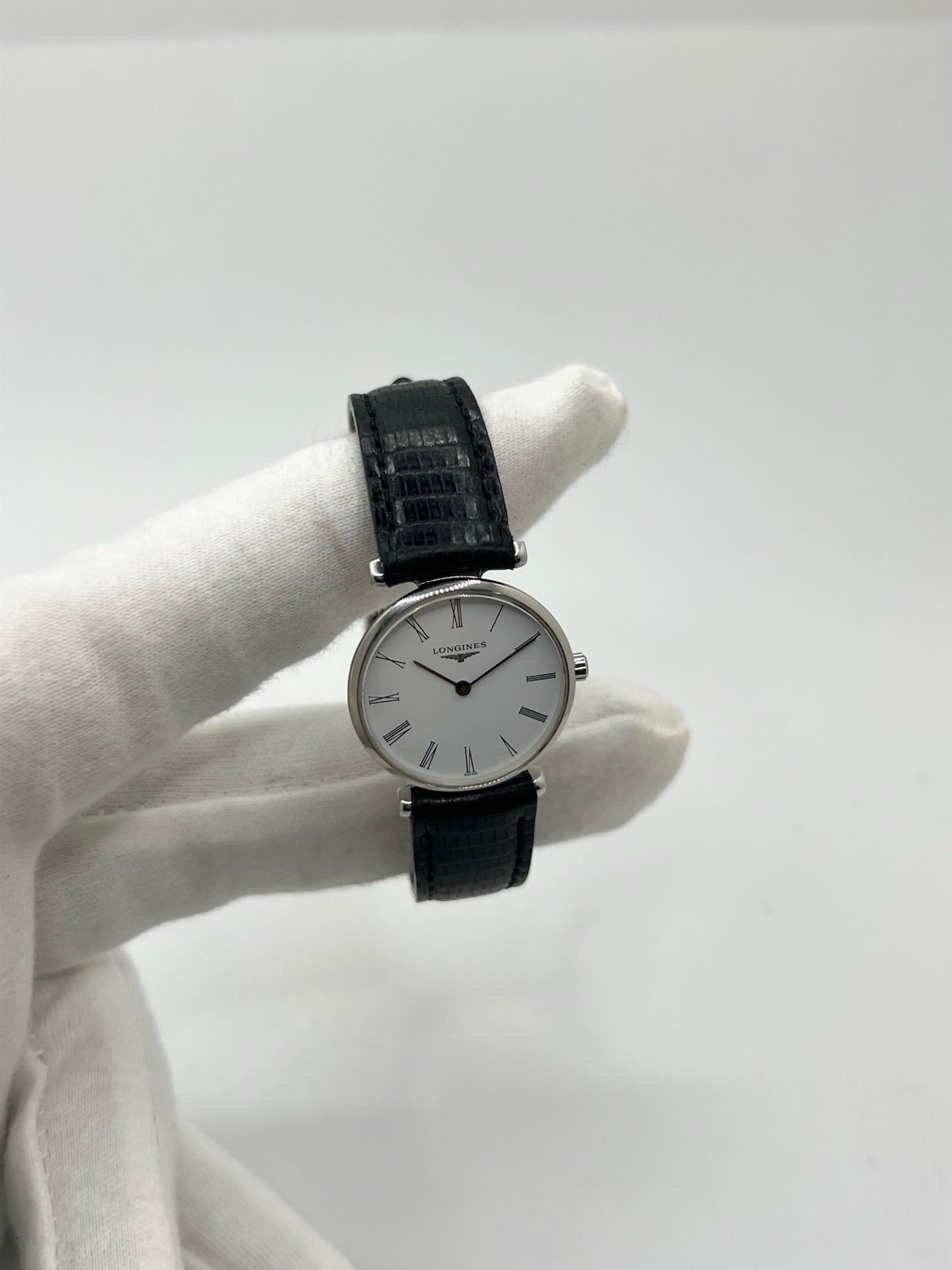 Montre Longines La Grande Classique L4.209.4 pour femme en acier avec bracelet en cuir de lézard noir. Ce modèle à mouvement quartz est doté d'un boîtier de 24 mm, d'un cadran blanc épuré sans chiffres, d'une lunette en acier et d'un verre saphir. Élégante et intemporelle, cette montre de luxe d'occasion est en très bon état avec de légères traces d'usure. Son design raffiné en fait un choix idéal pour un usage quotidien ou une collection horlogère.