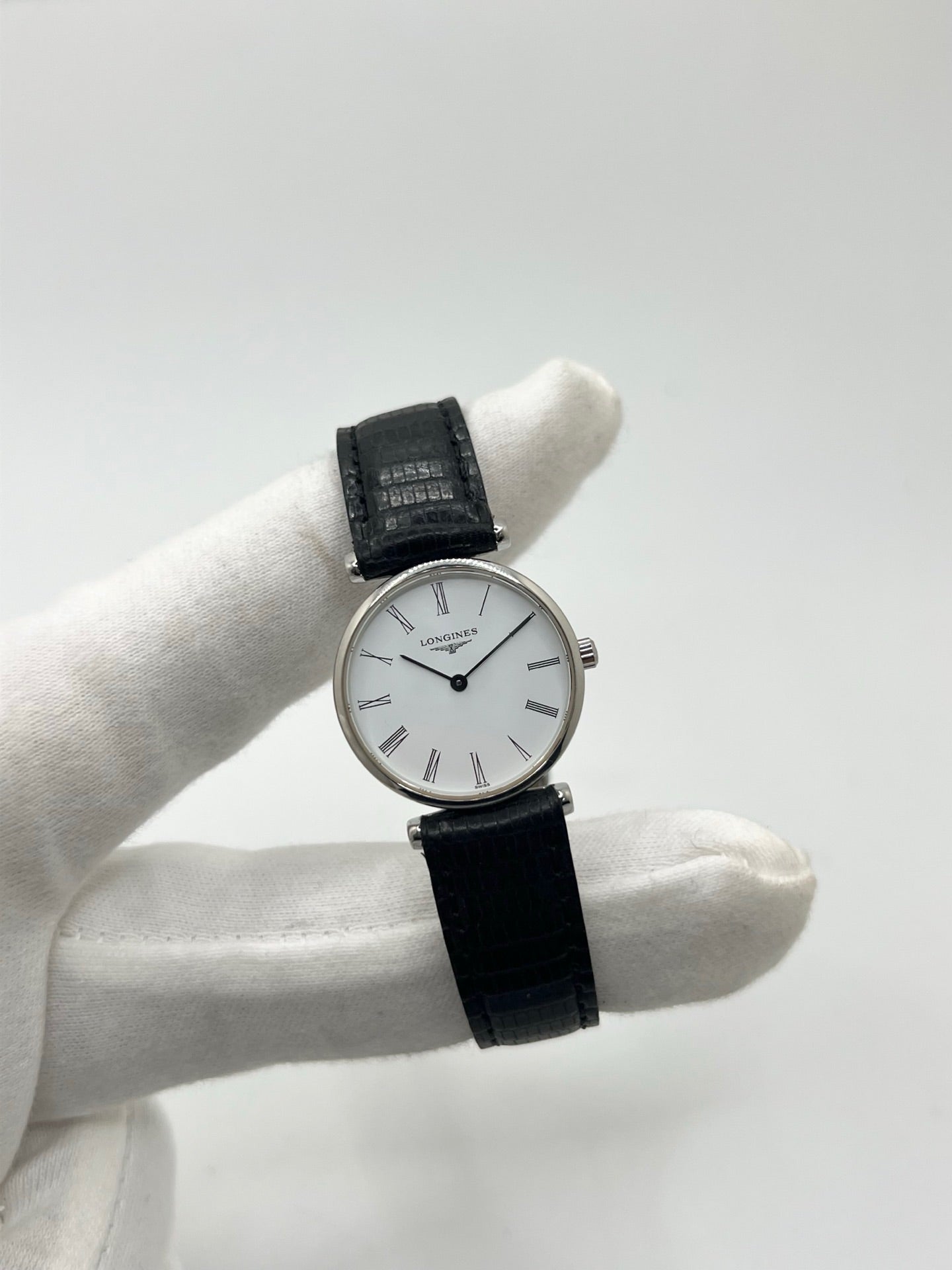 Montre Longines La Grande Classique L4.209.4 pour femme en acier avec bracelet en cuir de lézard noir. Ce modèle à mouvement quartz est doté d'un boîtier de 24 mm, d'un cadran blanc épuré sans chiffres, d'une lunette en acier et d'un verre saphir. Élégante et intemporelle, cette montre de luxe d'occasion est en très bon état avec de légères traces d'usure. Son design raffiné en fait un choix idéal pour un usage quotidien ou une collection horlogère.