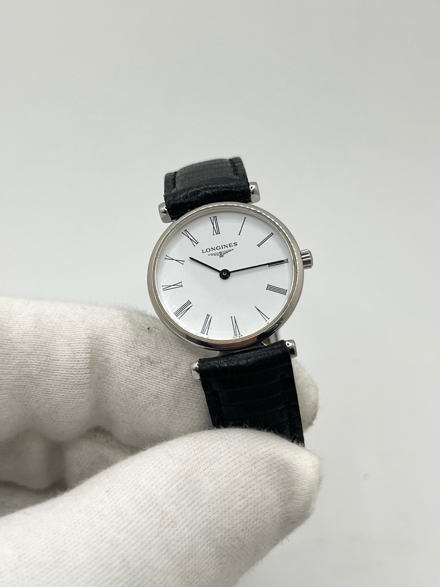 Montre Longines La Grande Classique L4.209.4 pour femme en acier avec bracelet en cuir de lézard noir. Ce modèle à mouvement quartz est doté d'un boîtier de 24 mm, d'un cadran blanc épuré sans chiffres, d'une lunette en acier et d'un verre saphir. Élégante et intemporelle, cette montre de luxe d'occasion est en très bon état avec de légères traces d'usure. Son design raffiné en fait un choix idéal pour un usage quotidien ou une collection horlogère.