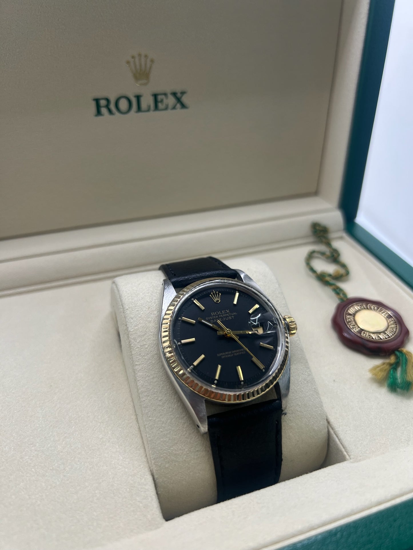 Montre Rolex Datejust automatique vintage de 36 mm en acier avec lunette en or jaune, cadran noir épuré sans chiffres et affichage de la date à 3 heures. Boîtier élégant protégé par un verre plexiglas, étanche jusqu’à 10 ATM. Bracelet en cuir noir avec boucle en acier. Mouvement mécanique à remontage automatique offrant environ 40 heures de réserve de marche. Modèle des années 1960, en très bon état, présentant de légères traces d’usure superficielles.