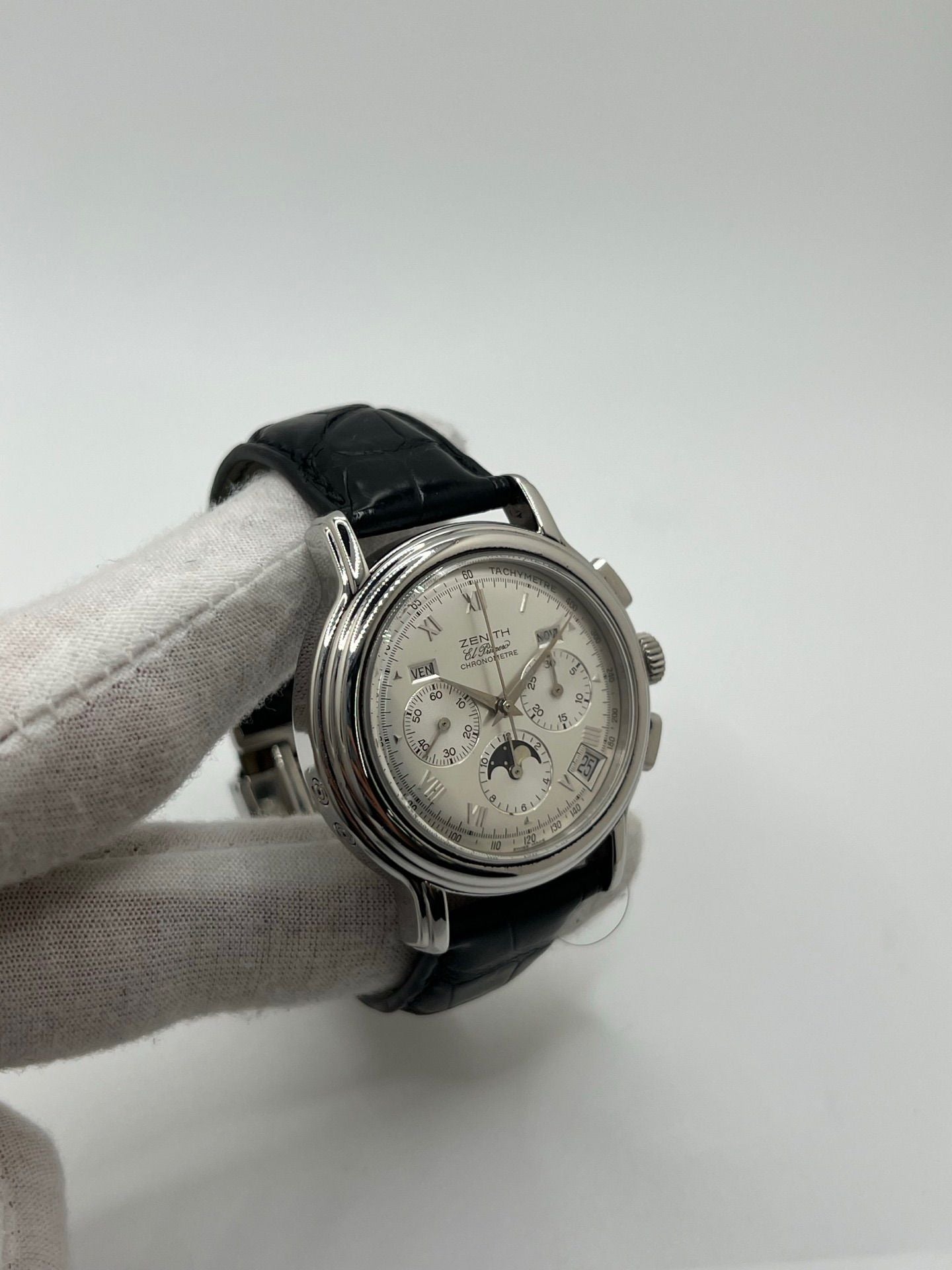 Montre chronographe automatique en acier avec cadran argenté à chiffres romains, fonction phase lunaire, date, jour et mois. Boîtier de 40 mm, verre saphir, fond transparent et bracelet en cuir noir. Modèle de haute précision doté du calibre 410 avec 50 heures de réserve de marche. Montre élégante pour homme ou unisexe.