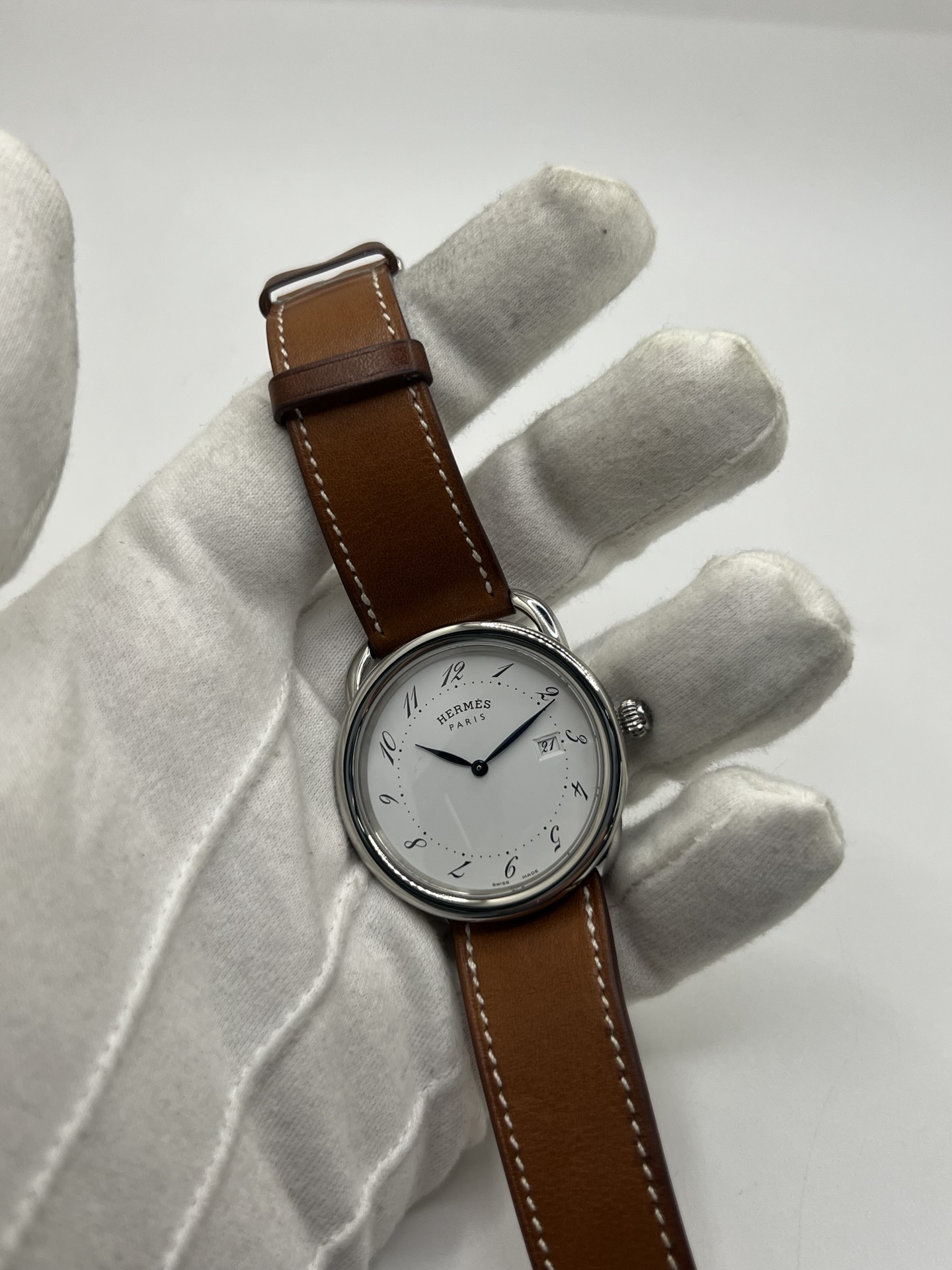 Montre Hermès Arceau Grand Modèle AR5.710 de 2014 en acier 38 mm avec mouvement quartz, cadran blanc à chiffres arabes et bracelet cuir brun d’origine. Cette montre de luxe Hermès Full Set avec boîte et papiers possède un verre saphir, une boucle ardillon acier et le design emblématique Arceau inspiré de l’univers équestre. Montre vintage Hermès élégante, révisée en 2026 et garantie 1 an.