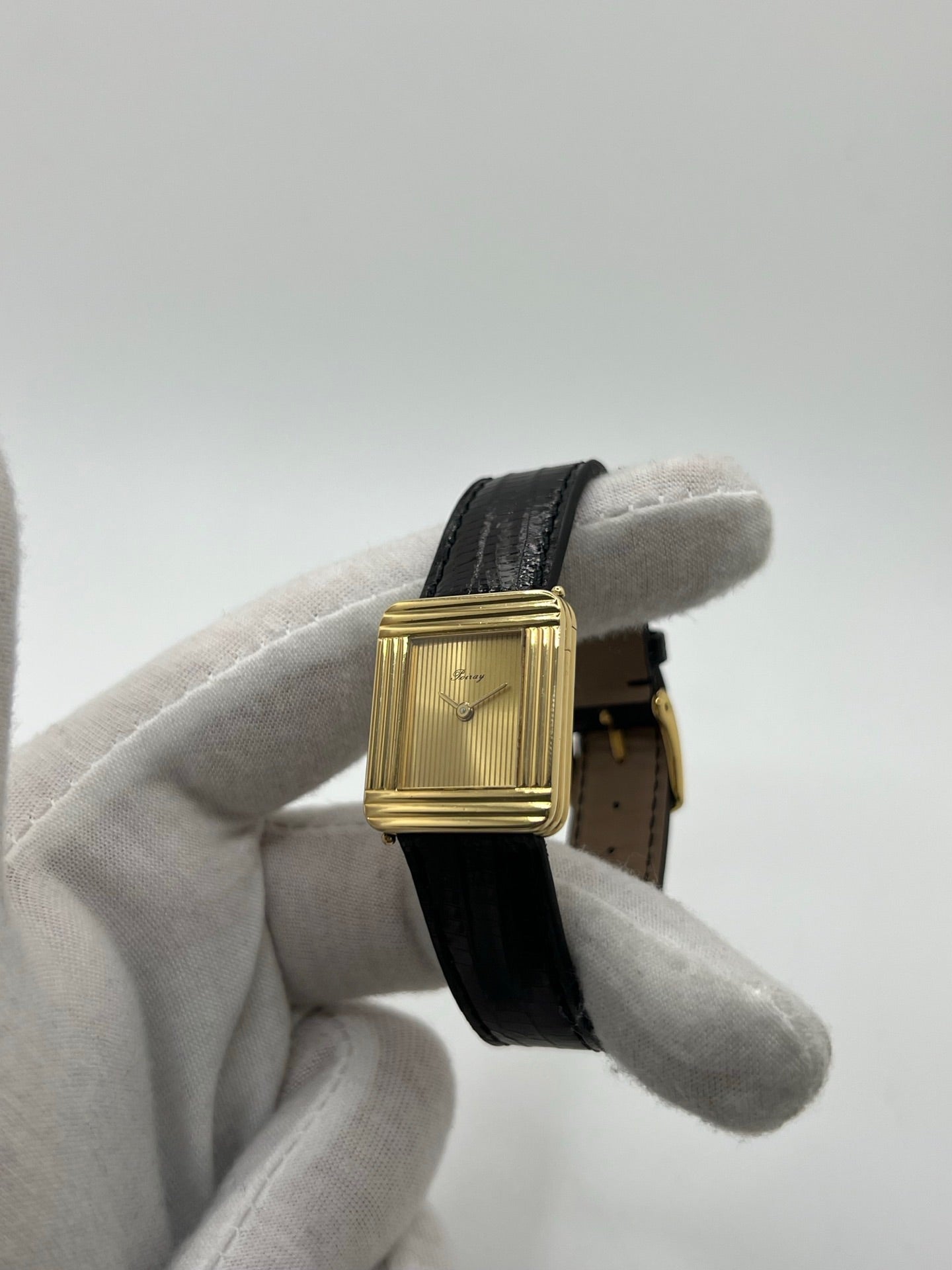 Montre femme Poiray Ma Première en or jaune 18K avec boîtier rectangulaire 22 x 26 mm, cadran doré sans chiffres et verre saphir. Modèle élégant équipé d’un mouvement quartz, bracelet en cuir noir et boucle en acier. Pièce d’occasion en très bon état présentant de légères traces d’usure non perceptibles. Montre raffinée, révisée récemment, idéale pour un style intemporel.