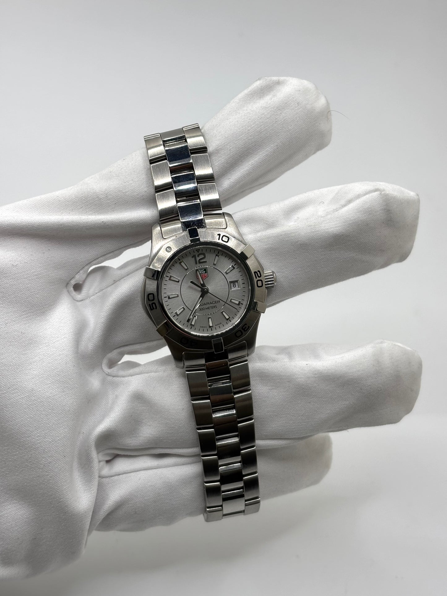 Montre femme TAG Heuer Aquaracer Lady référence WAF1412 en acier avec boîtier 27 mm et bracelet acier. Cadran argent avec chiffres arabes, mouvement quartz précis et étanchéité 30 ATM. Montre de luxe sportive et élégante en très bon état, révisée en 2026, idéale pour un usage quotidien ou une tenue habillée. Détail du boîtier acier poli, montre horlogère suisse féminine, intemporelle et raffinée.