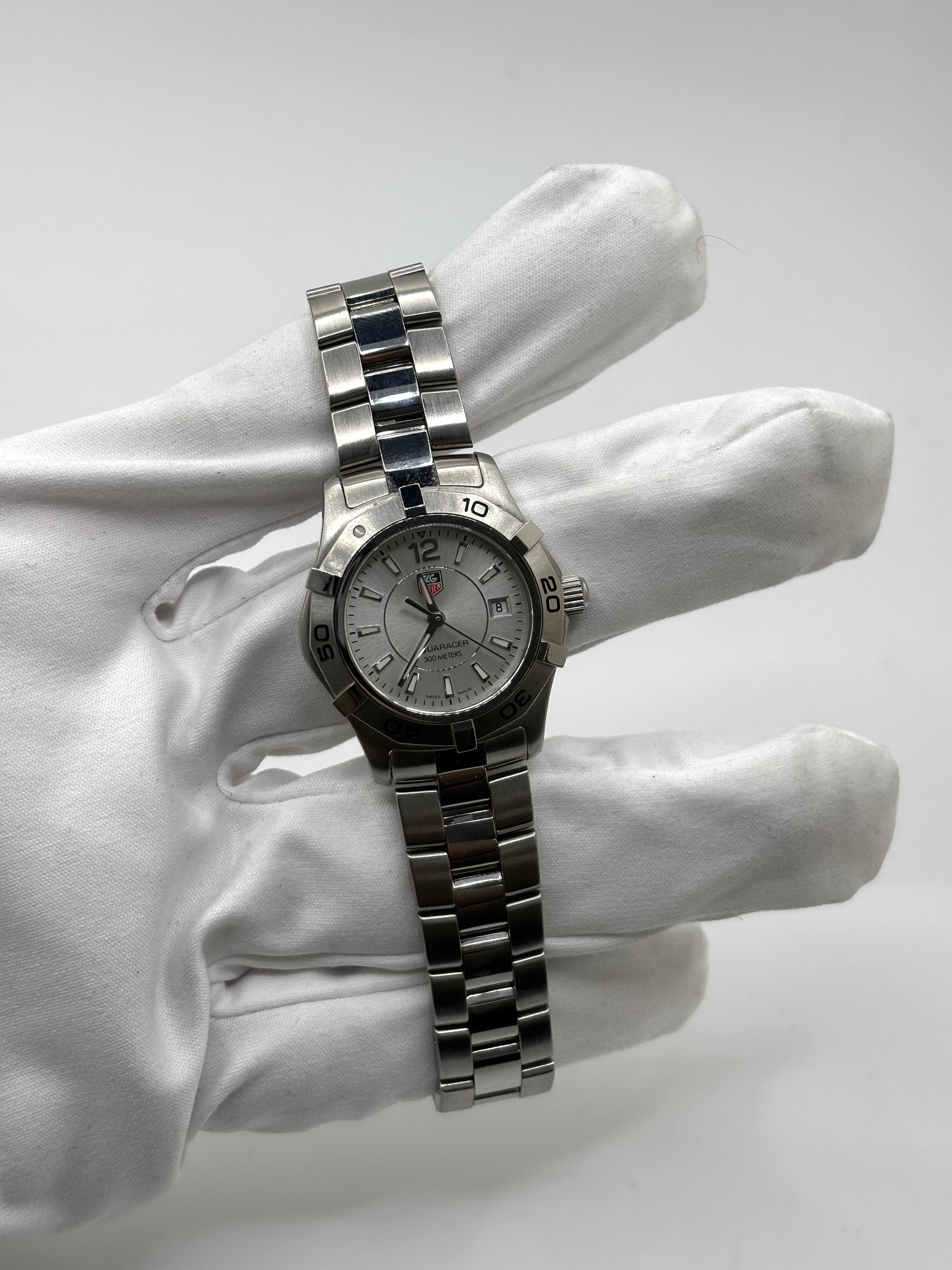 Montre femme TAG Heuer Aquaracer Lady référence WAF1412 en acier avec boîtier 27 mm et bracelet acier. Cadran argent avec chiffres arabes, mouvement quartz précis et étanchéité 30 ATM. Montre de luxe sportive et élégante en très bon état, révisée en 2026, idéale pour un usage quotidien ou une tenue habillée. Détail du boîtier acier poli, montre horlogère suisse féminine, intemporelle et raffinée.