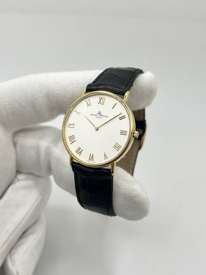 Montre Baume & Mercier Classima 15172A en or jaune, équipée d’un mouvement à quartz et d’un boîtier de 33 mm. Son cadran blanc à chiffres romains apporte une allure élégante et intemporelle, tandis que le verre saphir assure sa protection. Ce modèle est monté sur un bracelet noir en cuir de crocodile avec boucle ardillon en acier. Une montre raffinée, idéale pour une tenue chic et élégante, en très bon état.