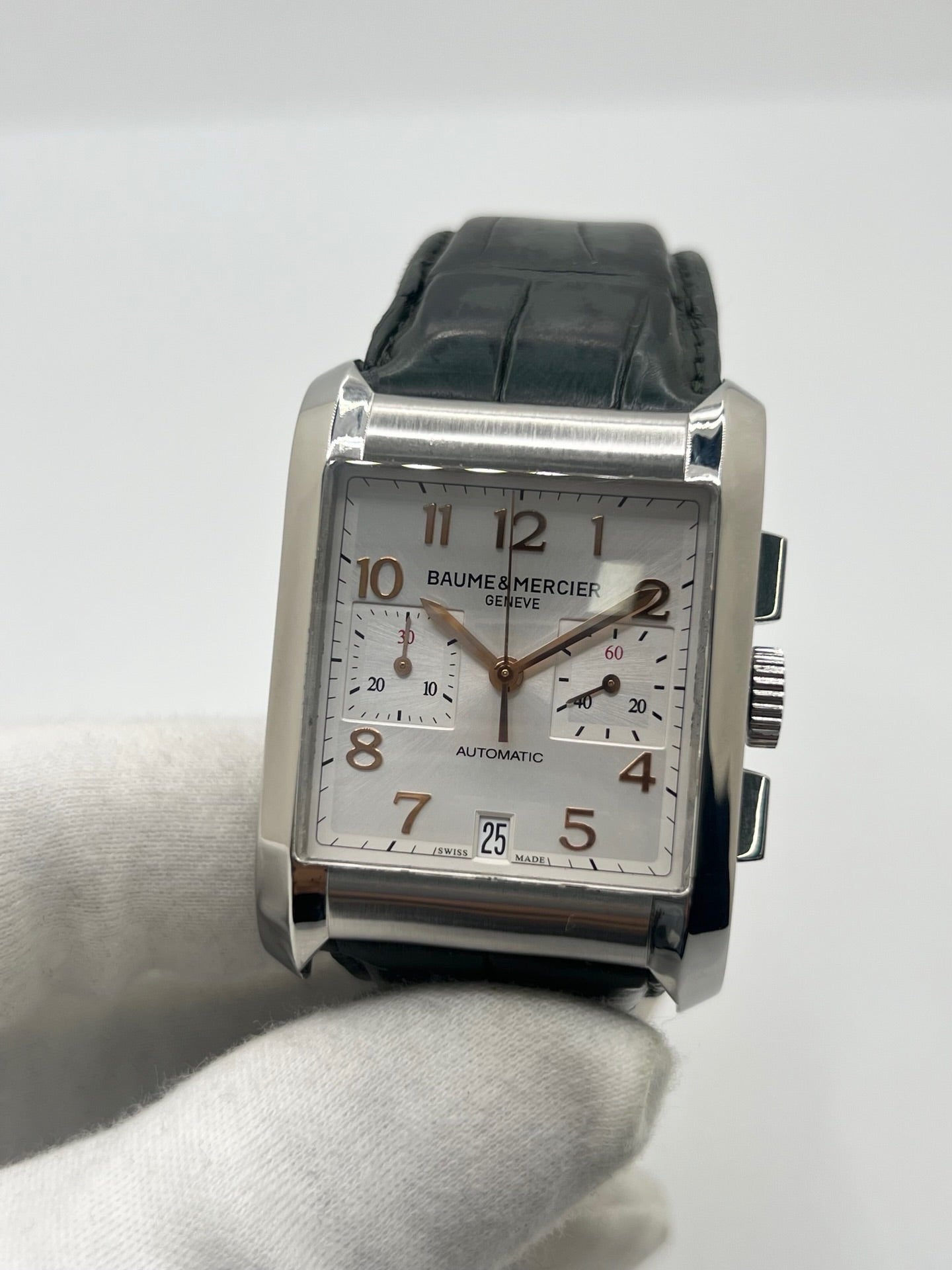 Montre Baume & Mercier Hampton réf. 65698, modèle automatique pour homme ou unisexe. Boîtier en acier de 34,5 mm avec verre saphir résistant aux rayures. Cadran argent avec index en chiffres arabes, offrant une lecture élégante et classique. Bracelet en cuir vert avec boucle déployante en acier. Fonction chronographe et date. Montre de luxe d’occasion en très bon état, avec légères traces d’usure. Révisée le 24 juin 2026 en interne. Livrée sans coffret ni papiers. Disponible à Paris.