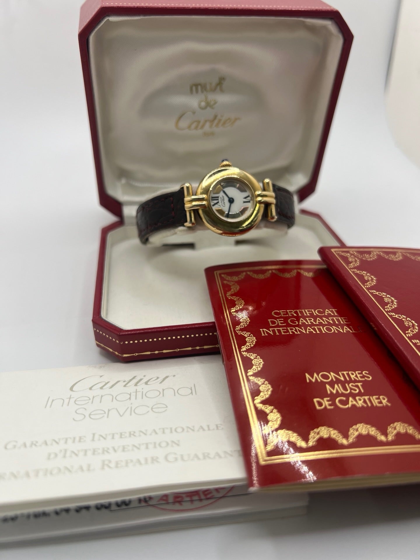 Montre femme Cartier Colisée réf. 590002 en argent avec mouvement quartz. Modèle vintage de 1995 au cadran blanc à chiffres romains et bracelet en cuir or. Verre saphir, boucle ardillon en argent. Élégance intemporelle signée Cartier, livrée avec coffret et papiers d’origine. Montre d’occasion en bon état, révisée en 2025.