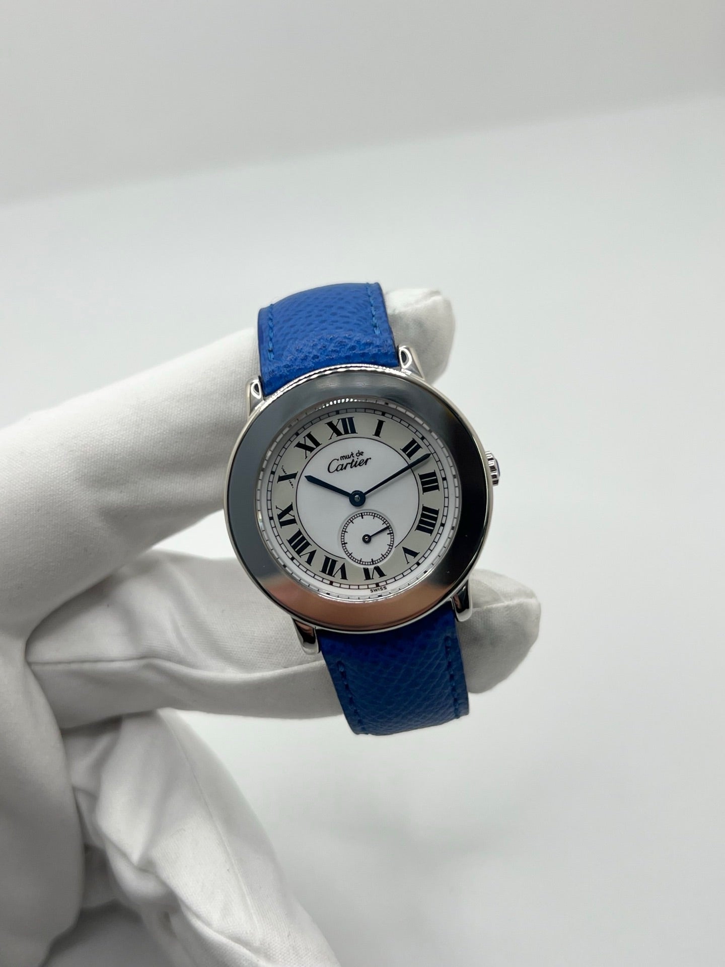 Montre Cartier Must de Cartier Ronde, modèle femme élégant à mouvement quartz. Boîtier rond en métal précieux, cadran blanc raffiné avec chiffres romains, design classique signature Cartier. Bracelet cuir bleu avec boucle ardillon en acier. Verre saphir résistant, diamètre 33 mm. Montre de luxe d’occasion en très bon état, avec légères traces d’usage peu visibles. Révisée en interne le 22 avril 2026. Livrée avec coffret d’origine, sans papiers, disponible à Paris.
