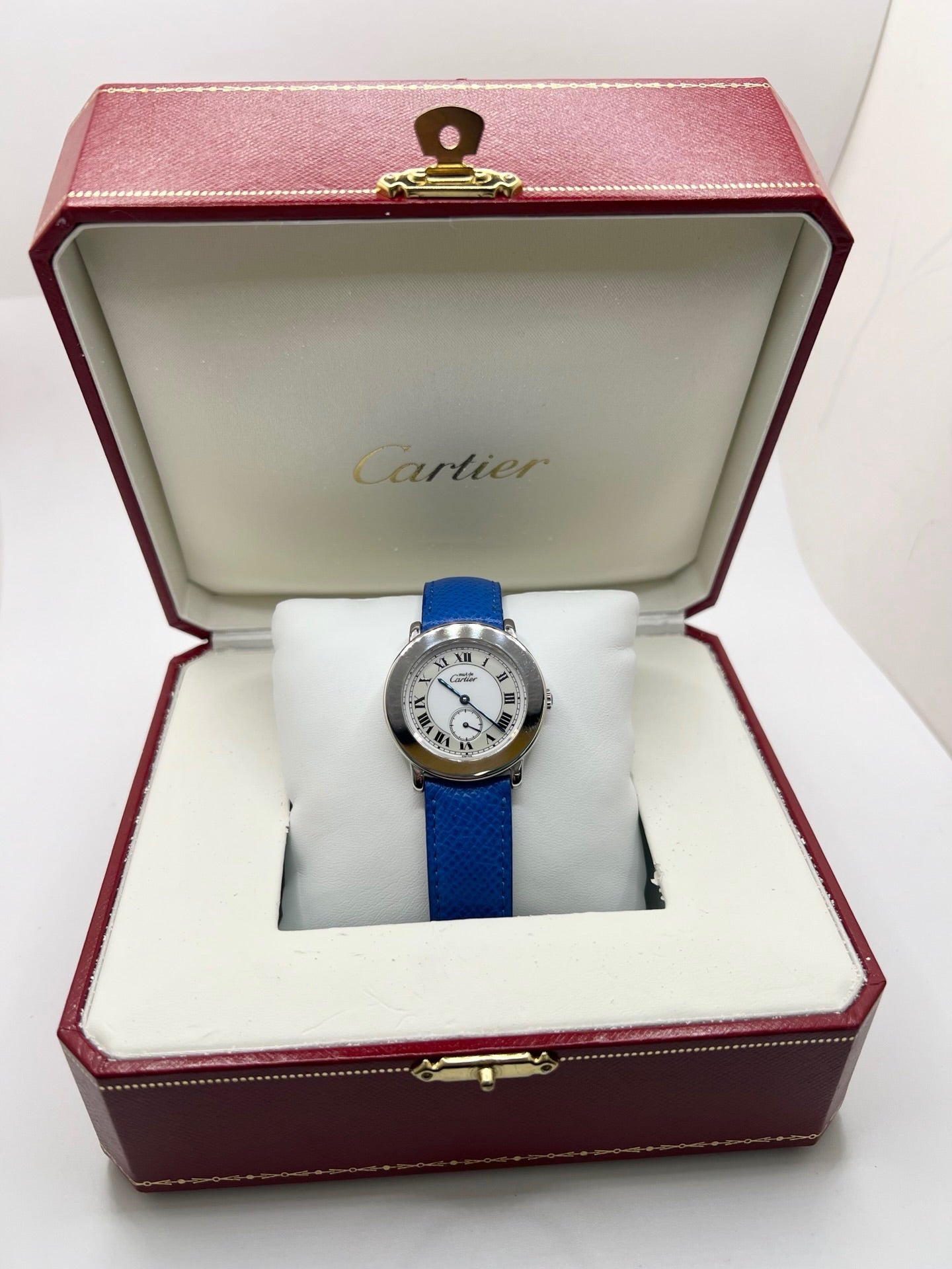 Montre Cartier Must de Cartier Ronde, modèle femme élégant à mouvement quartz. Boîtier rond en métal précieux, cadran blanc raffiné avec chiffres romains, design classique signature Cartier. Bracelet cuir bleu avec boucle ardillon en acier. Verre saphir résistant, diamètre 33 mm. Montre de luxe d’occasion en très bon état, avec légères traces d’usage peu visibles. Révisée en interne le 22 avril 2026. Livrée avec coffret d’origine, sans papiers, disponible à Paris.
