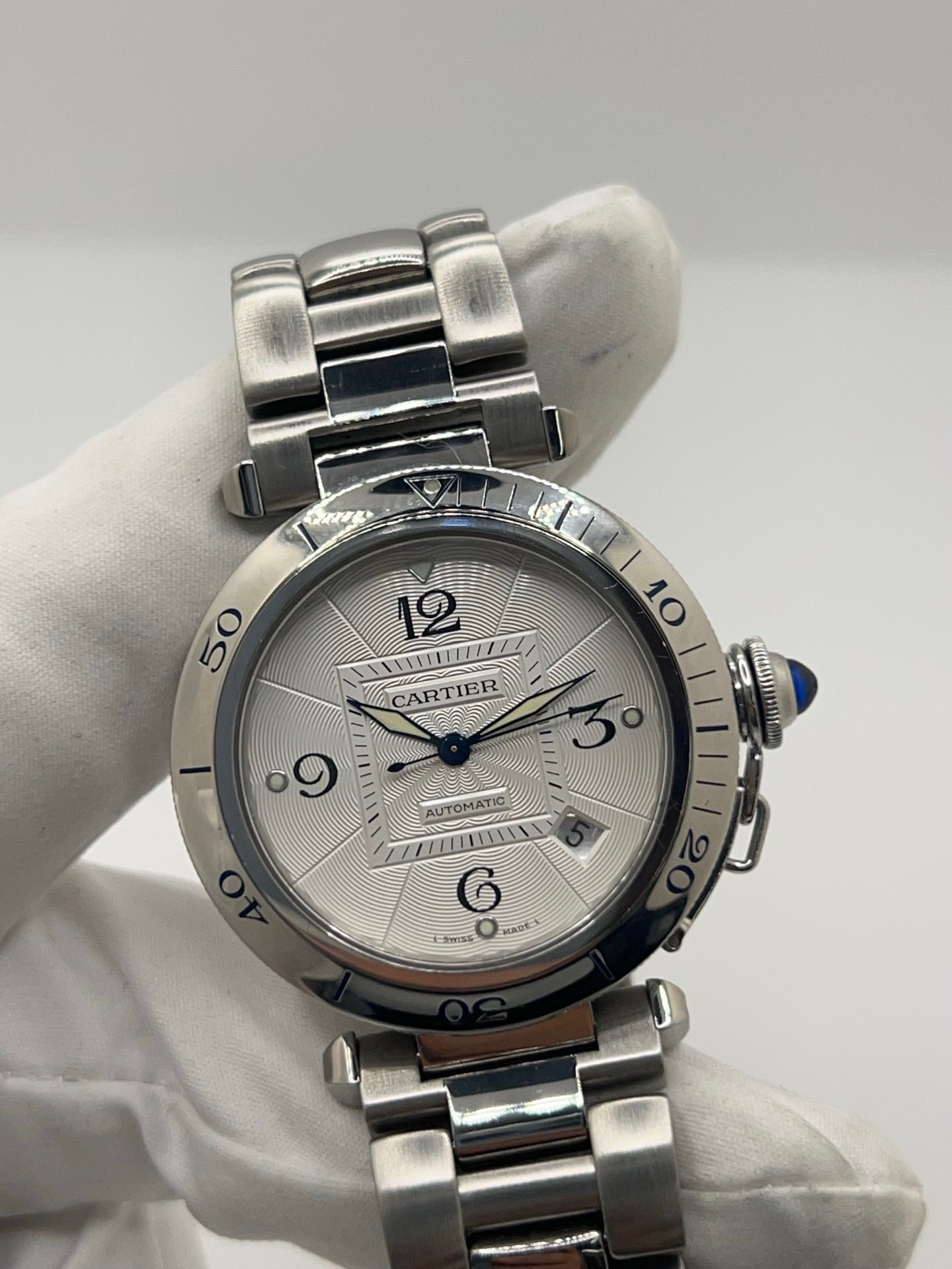 Montre Cartier Pasha automatique en acier, boîtier 38 mm avec verre saphir et cadran argent à chiffres arabes. Équipée d’un mouvement automatique calibre Cartier 191 avec fonction date. Bracelet acier avec boucle déployante. Modèle d’occasion en très bon état, révisé, présentant de légères micro-rayures peu visibles. Montre élégante et sportive, adaptée à un usage quotidien, livrée avec son coffret d’origine.
