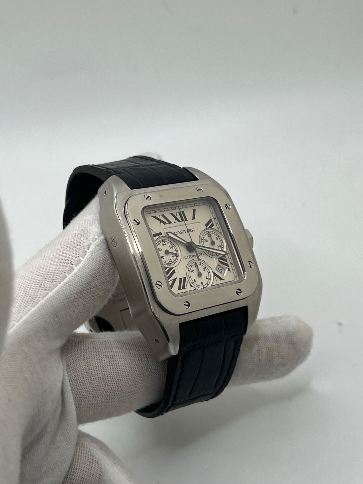 Montre Cartier Santos 100 XL Chronograph pour homme, modèle emblématique au design sport-chic. Boîtier en acier, cadran blanc à chiffres romains, bracelet en cuir noir. Mouvement automatique précis avec chronographe et date. Montre d’occasion en excellent état, révisée, livrée avec coffret d’origine.