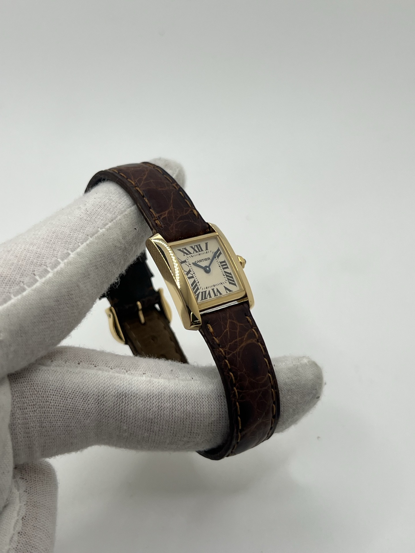 Montre Cartier Tank Française référence 1820 en or jaune 18K, petit modèle pour femme, boîtier rectangulaire emblématique aux lignes droites et élégantes, cadran blanc avec chiffres romains noirs, minuterie chemin de fer et aiguilles bleuies en forme de glaive. Bracelet intégré en acier avec boucle déployante. Mouvement quartz précis. Montre de luxe intemporelle, raffinée et iconique, idéale pour un porté quotidien ou une tenue habillée.