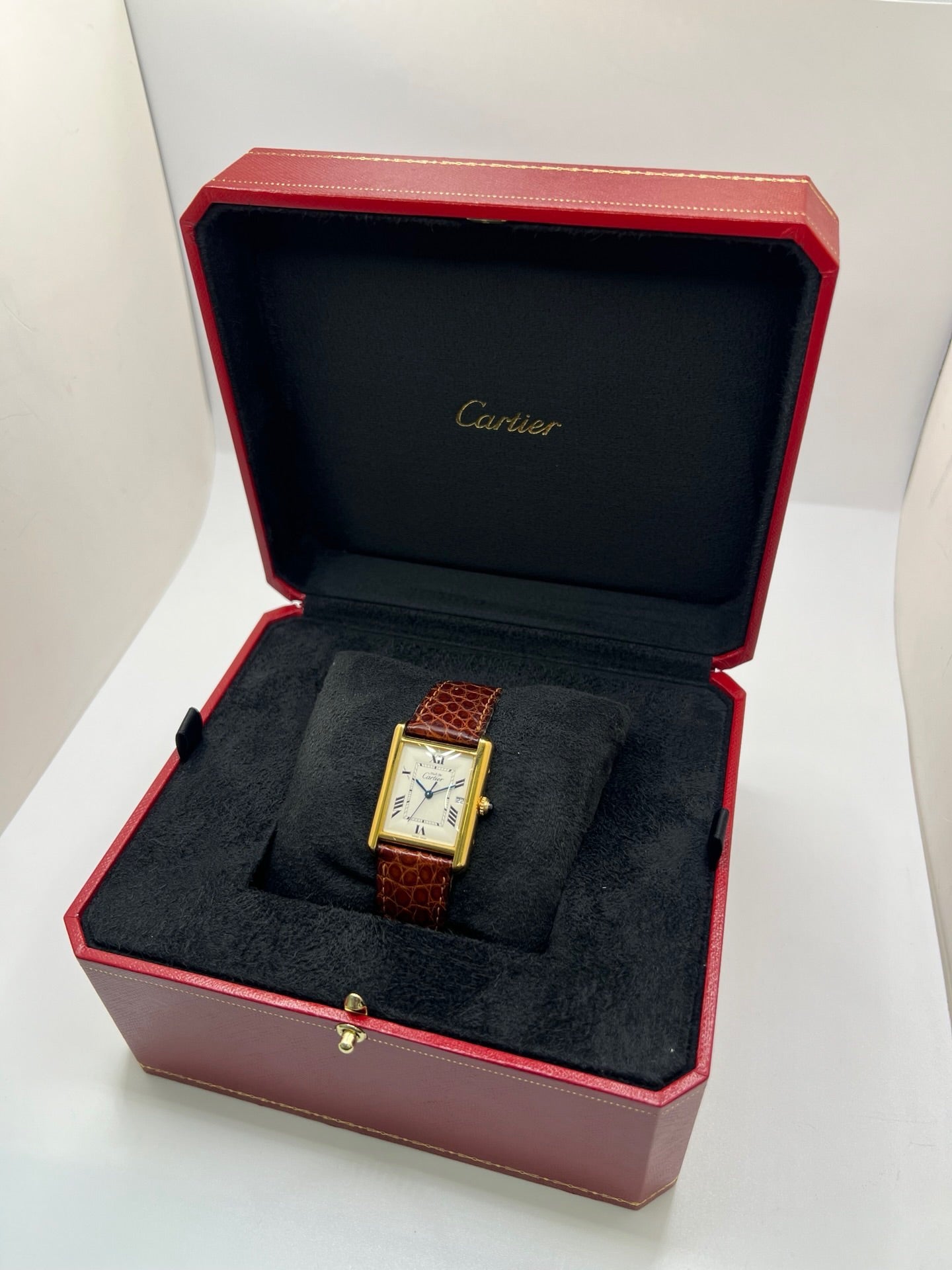 Montre Cartier Tank Must grand modèle en argent avec cadran blanc à chiffres romains, mouvement quartz et fonction date. Boîtier rectangulaire 25 x 33 mm avec verre minéral, bracelet en cuir brun et boucle ardillon en acier. Modèle iconique au design élégant et intemporel, idéal pour homme ou unisexe. Montre d’occasion en bon état, révisée, avec coffret d’origine.