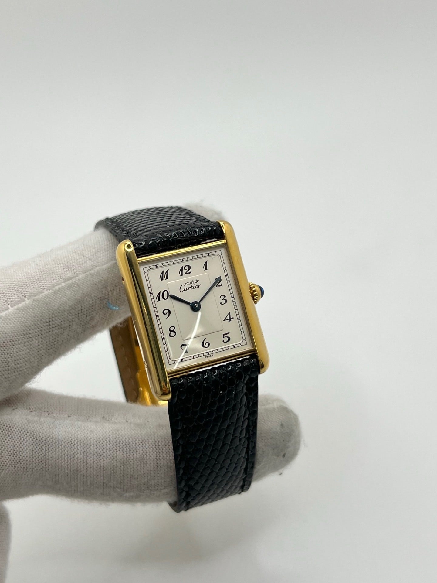 Montre Cartier Tank Vermeil référence 590005 vintage de 1989, avec boîtier rectangulaire en argent aux proportions classiques 23 x 30 mm, cadran argenté élégant avec chiffres arabes noirs et aiguilles bleuies, verre saphir et mouvement quartz. Montée sur un bracelet en cuir de lézard noir avec boucle ardillon en acier. Modèle iconique au design intemporel, livré avec son coffret et ses papiers d’origine, en très bon état.