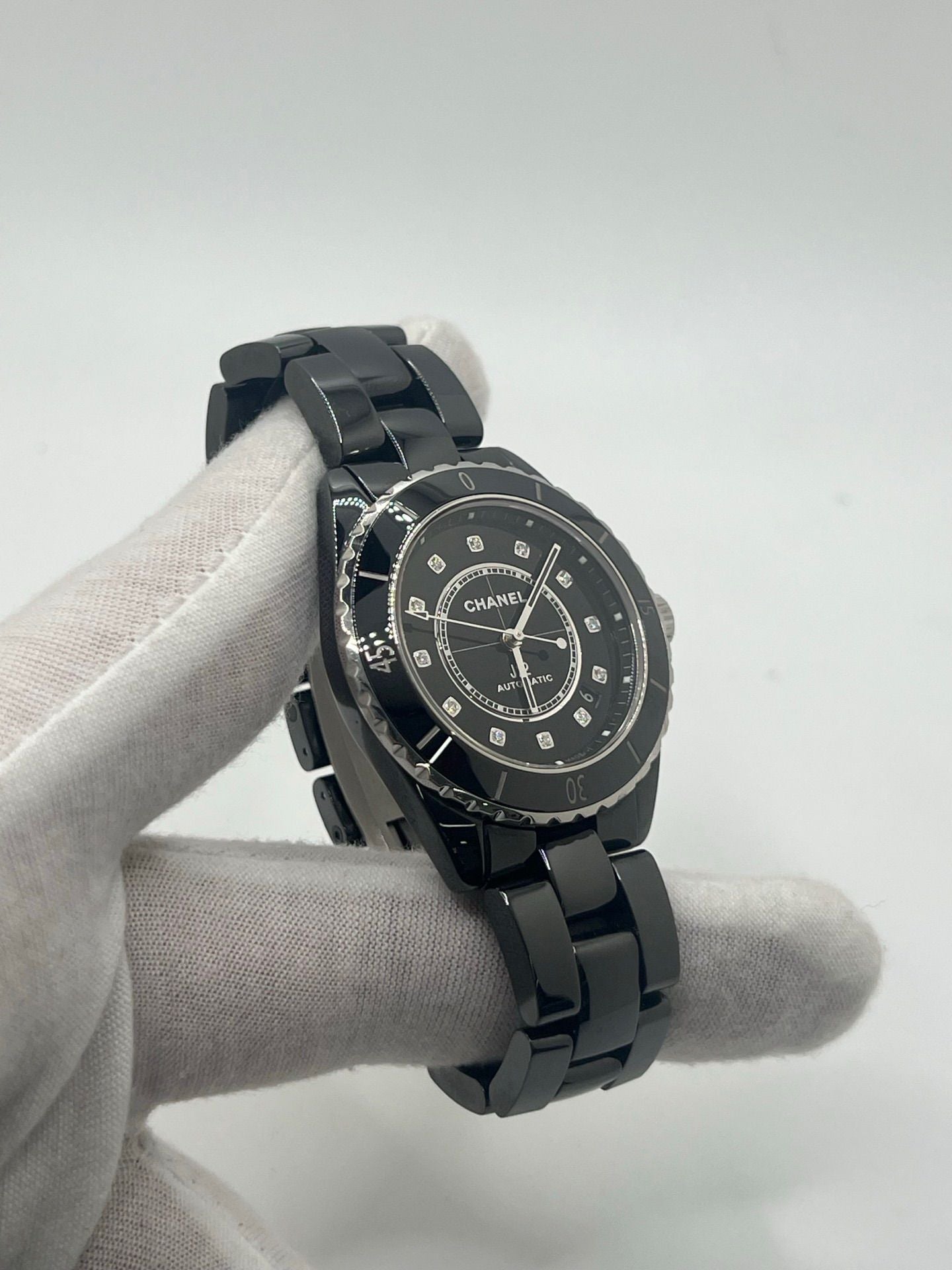 Montre Chanel J12 12.1 en céramique noire avec sertissage de diamants, alliant élégance et performance. Mouvement automatique de précision, boîtier de 38 mm et verre saphir. Modèle de luxe d'occasion en excellent état, livré avec coffret d'origine. Idéal pour collectionneurs et amateurs de haute horlogerie.