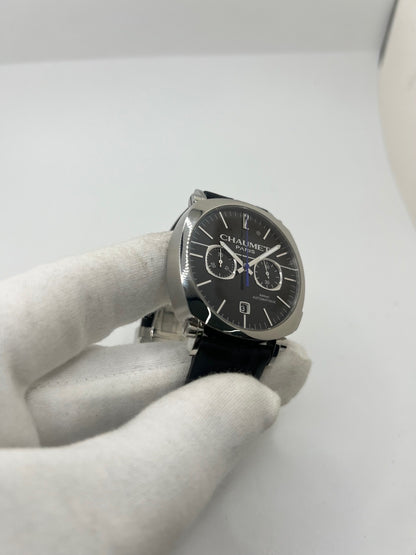 Montre Chaumet Dandy réf. 1229 pour homme ou unisexe, dotée d’un mouvement automatique. Boîtier en acier de 40 mm avec lunette assortie et verre saphir résistant aux rayures. Cadran noir à index bâtons, fonction chronographe et affichage de la date. Bracelet en cuir noir avec boucle déployante en acier. Montre de luxe d’occasion en très bon état, présentant de légères traces d’usure. Révisée en interne le 23 juin 2026, livrée avec coffret d’origine, sans papiers. Disponible à Paris. 