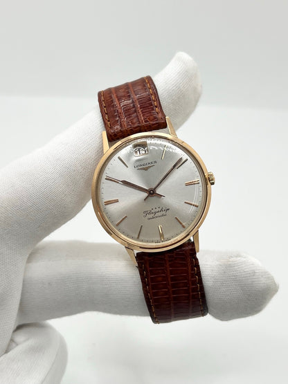 Montre Longines Flagship 2407 vintage en très bon état, datant approximativement de 1962, avec mouvement automatique calibre 341. Son boîtier de 35 mm en or rose est associé à un cadran argent à index bâtons et un verre Plexiglas. Cette Longines Flagship possède un bracelet en cuir de lézard brun avec boucle ardillon en acier. Elle dispose également d’une fonction date et d’un design élégant et intemporel.