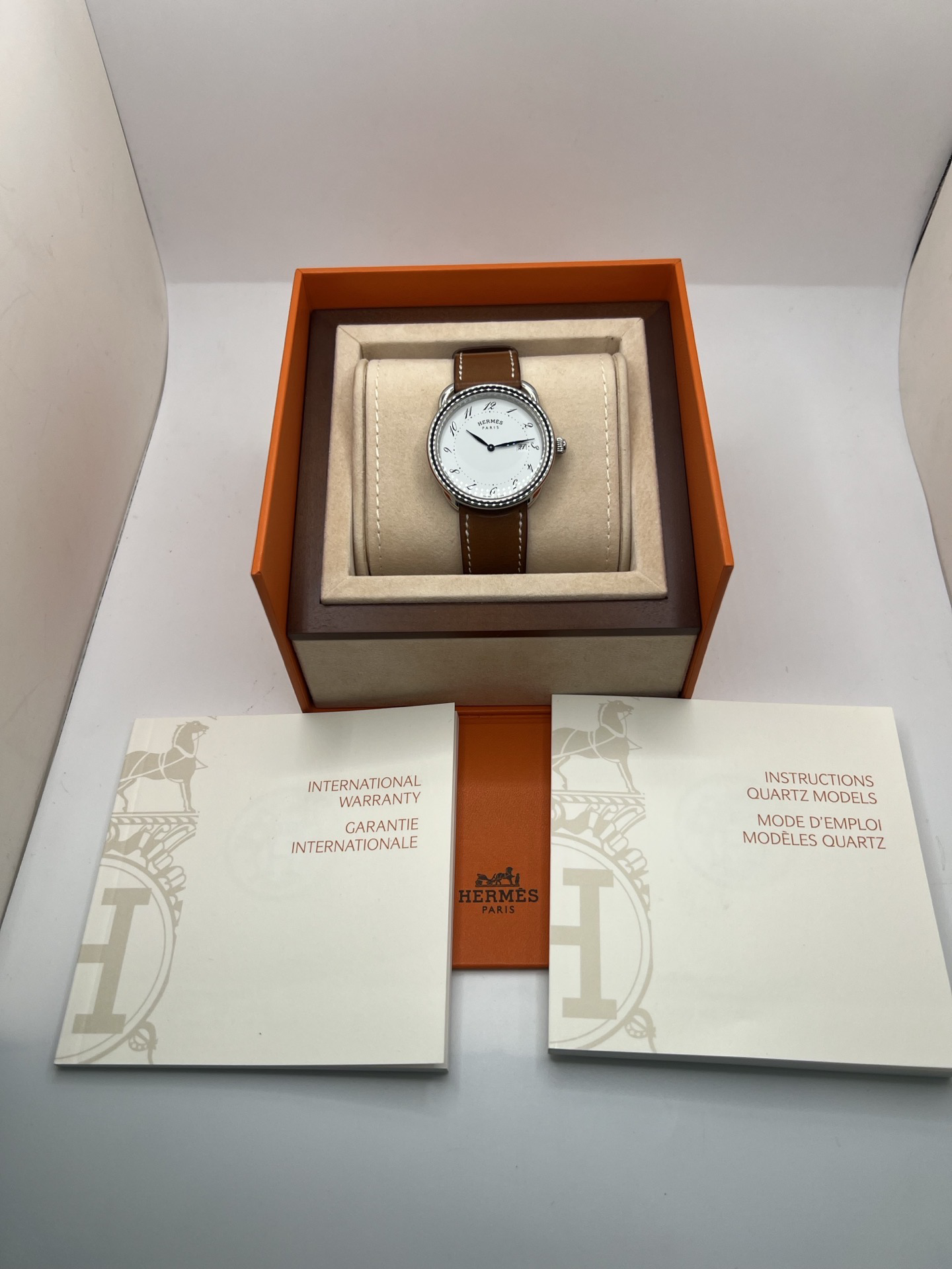 Montre Hermès Arceau Grand Modèle AR5.710 de 2014 en acier 38 mm avec mouvement quartz, cadran blanc à chiffres arabes et bracelet cuir brun d’origine. Cette montre de luxe Hermès Full Set avec boîte et papiers possède un verre saphir, une boucle ardillon acier et le design emblématique Arceau inspiré de l’univers équestre. Montre vintage Hermès élégante, révisée en 2026 et garantie 1 an.
