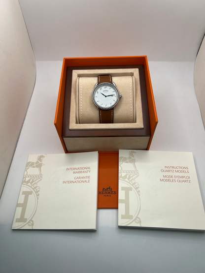 Montre Hermès Arceau Grand Modèle AR5.710 de 2014 en acier 38 mm avec mouvement quartz, cadran blanc à chiffres arabes et bracelet cuir brun d’origine. Cette montre de luxe Hermès Full Set avec boîte et papiers possède un verre saphir, une boucle ardillon acier et le design emblématique Arceau inspiré de l’univers équestre. Montre vintage Hermès élégante, révisée en 2026 et garantie 1 an.