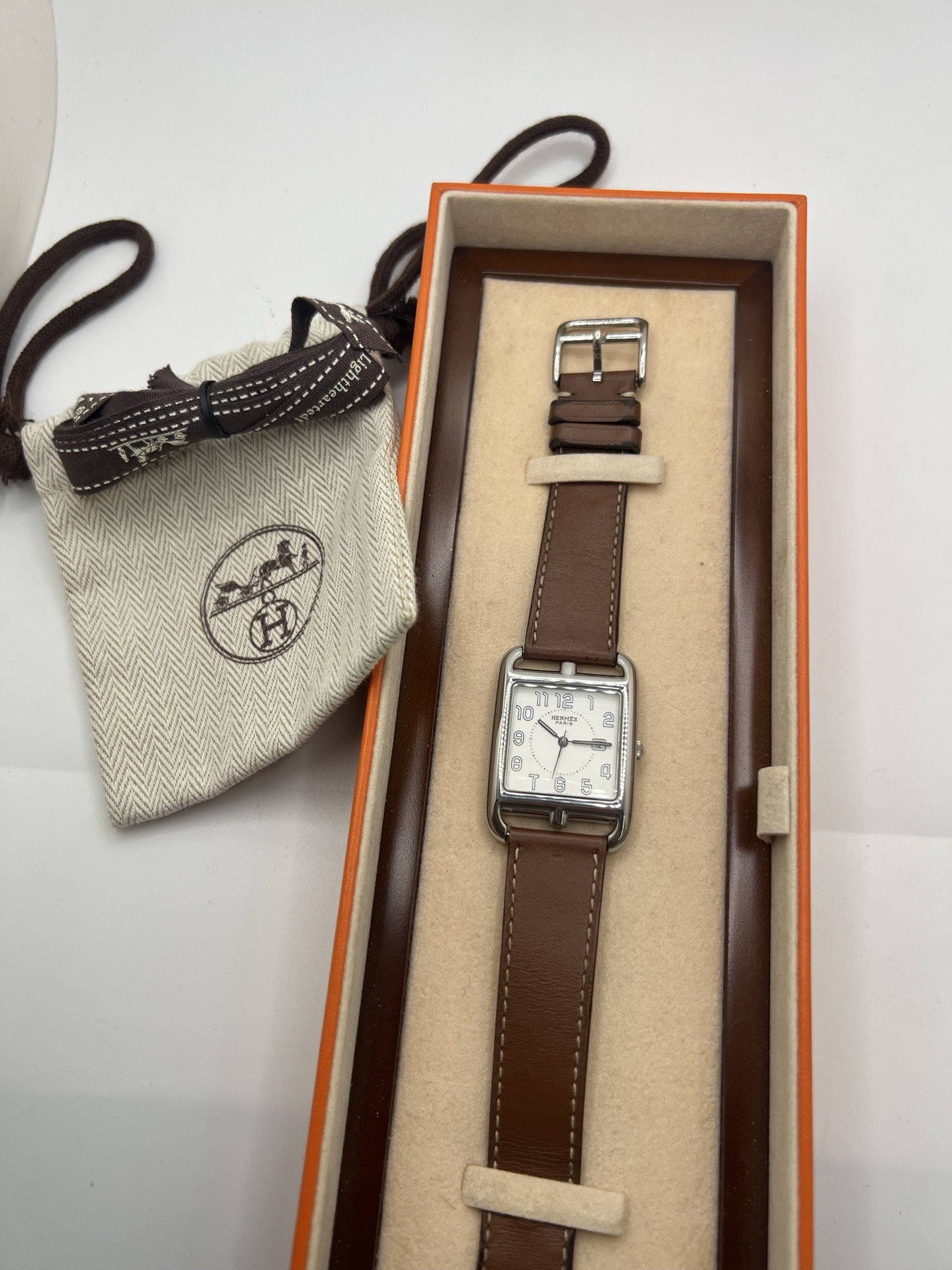 Montre Hermès Cape Cod Grand Modèle en acier inoxydable, boîtier rectangulaire iconique aux lignes élégantes et contemporaines, cadran argenté épuré avec chiffres arabes stylisés et aiguilles fines. Bracelet en cuir signature Hermès offrant confort et raffinement. Mouvement quartz précis. Montre de luxe intemporelle et sophistiquée, idéale pour un porté quotidien ou une tenue habillée, symbole du savoir-faire horloger et du style parisien.