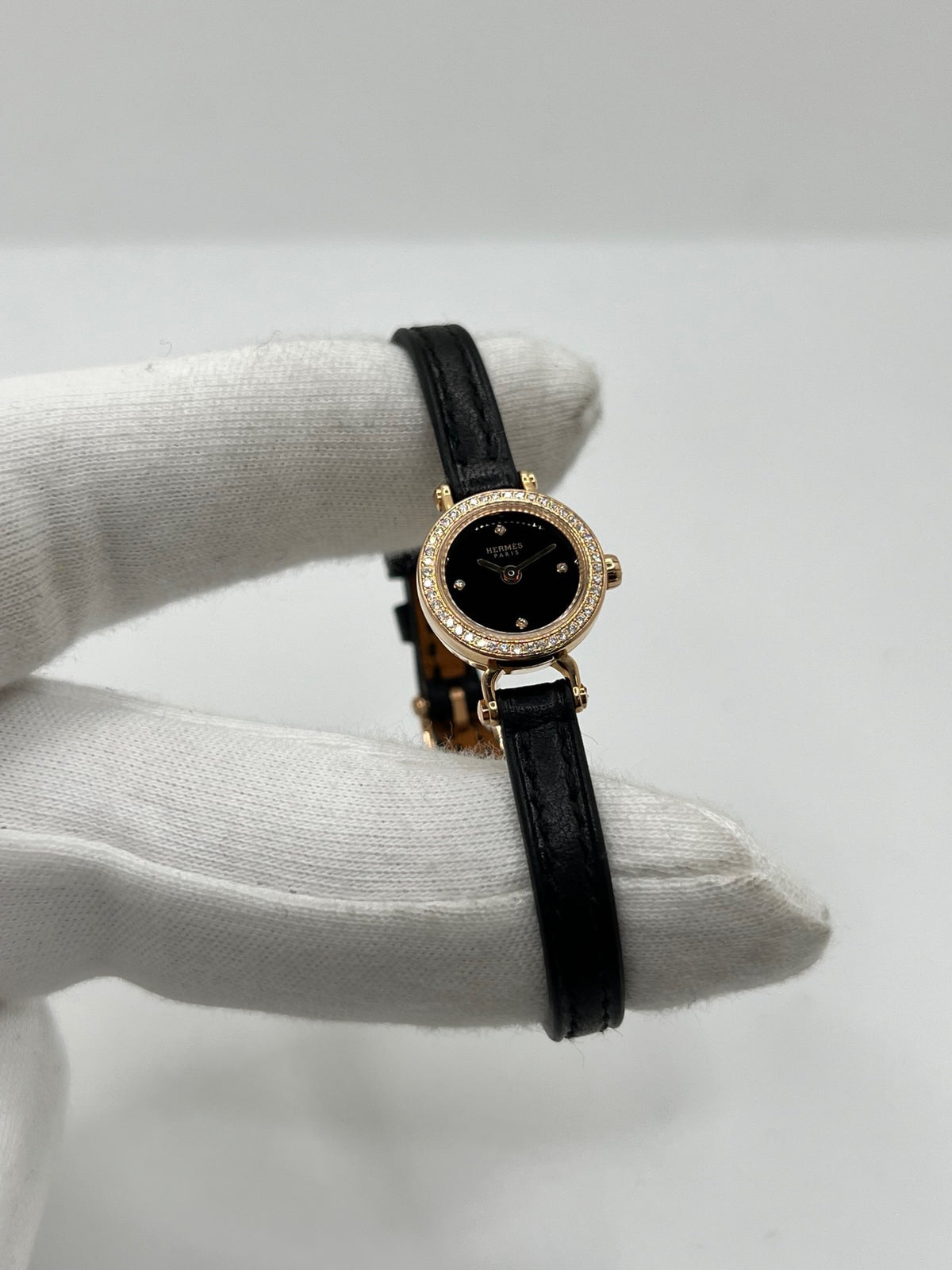 Montre Hermès Faubourg FG4.171 pour femme, dotée d’un élégant boîtier en or rose de 15,5 mm et d’un mouvement quartz. Elle se distingue par son cadran noir sans chiffres, protégé par un verre saphir, et son bracelet en cuir noir avec boucle ardillon en or rose. Cette montre de luxe Hermès associe raffinement, élégance et discrétion. Modèle d’occasion en très bon état, révisé en interne en octobre 2026 et livré avec son coffret d’origine.