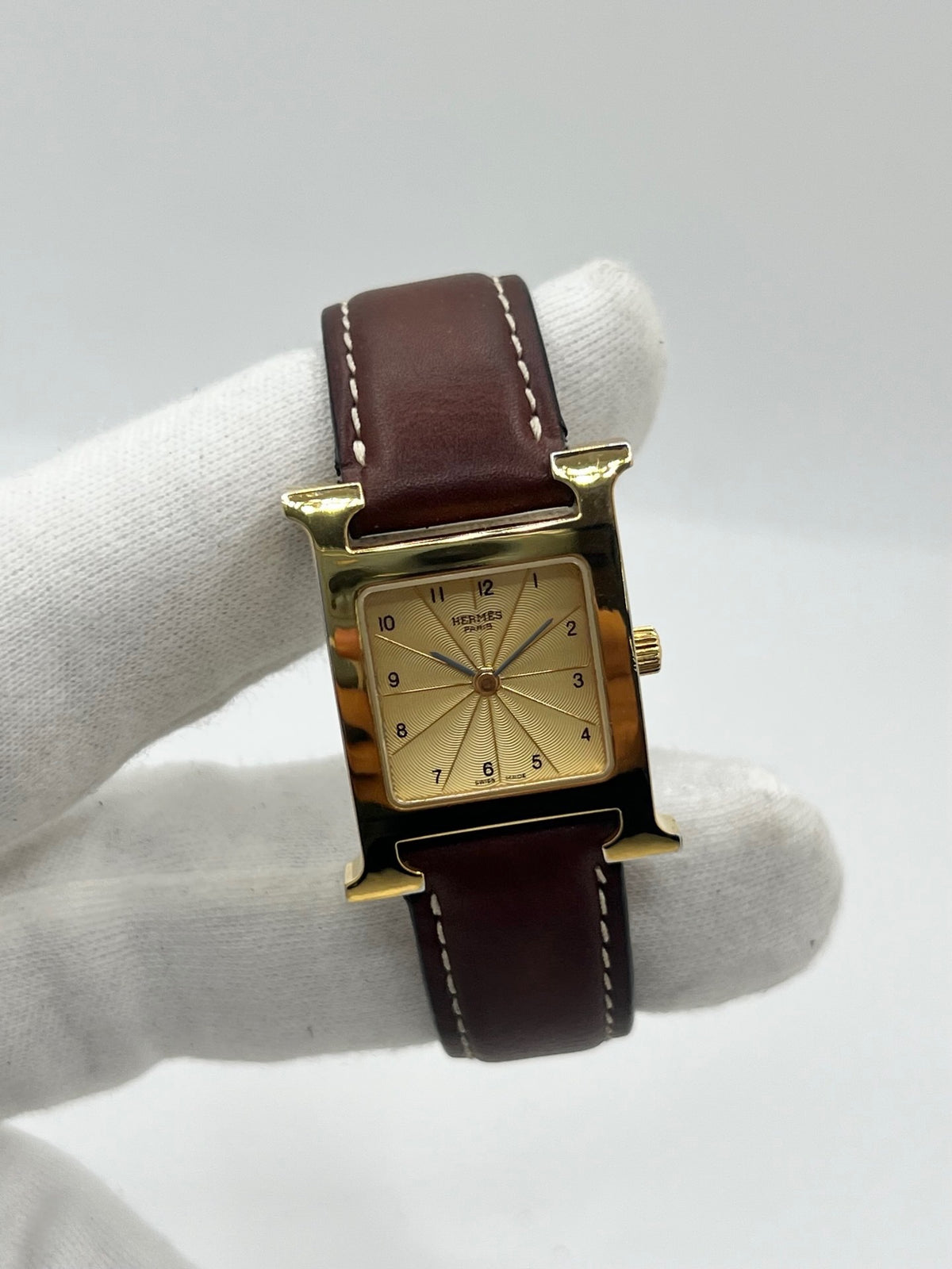 Montre Hermès Heure H HH1.201 pour femme, équipée d’un mouvement quartz et d’un boîtier en acier de 21 mm. Son cadran couleur or est protégé par un verre saphir et accompagné d’un bracelet brun en cuir de vache avec boucle ardillon en acier. Étanche à 3 ATM, cette montre Hermès Heure H se distingue par son célèbre boîtier en forme de H et son design élégant. En très bon état, elle présente de légères traces d’usure.
