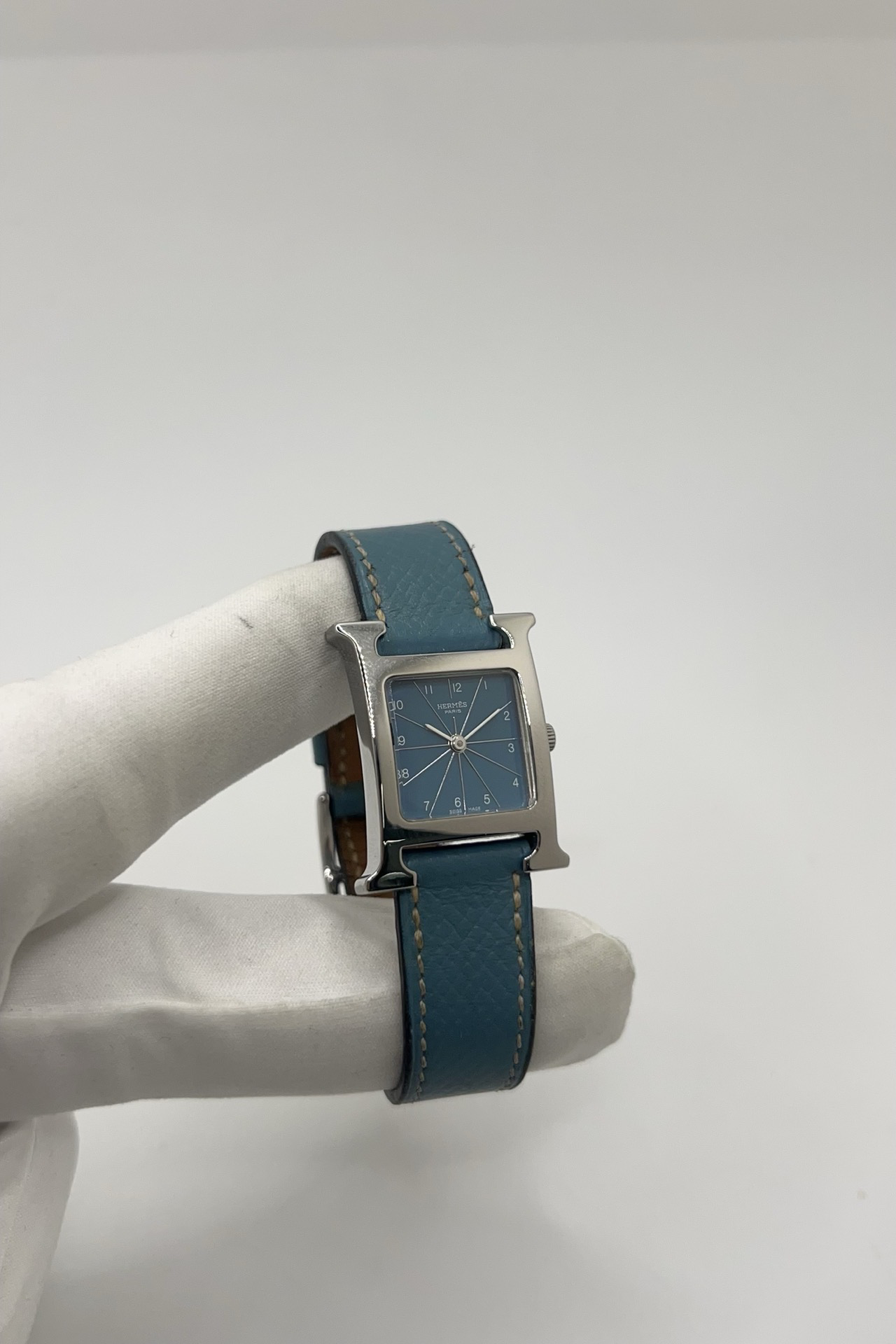 Montre Hermès Heure H HH1.210 en acier avec cadran bleu à chiffres arabes et bracelet cuir Hermès bleu d’origine. Cette montre Hermès femme quartz au design iconique en forme de H incarne l’élégance parisienne et le luxe discret. Modèle Hermès Heure H acier de 21 x 30 mm avec verre saphir, boucle ardillon acier et mouvement quartz fiable. Montre de luxe féminine chic et intemporelle, révisée et livrée avec certificat d’authenticité.