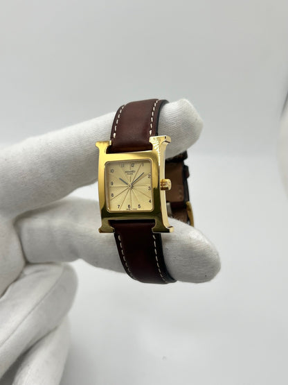 Montre Hermès Heure H HH1.201 pour femme, équipée d’un mouvement quartz et d’un boîtier en acier de 21 mm. Son cadran couleur or est protégé par un verre saphir et accompagné d’un bracelet brun en cuir de vache avec boucle ardillon en acier. Étanche à 3 ATM, cette montre Hermès Heure H se distingue par son célèbre boîtier en forme de H et son design élégant. En très bon état, elle présente de légères traces d’usure.
