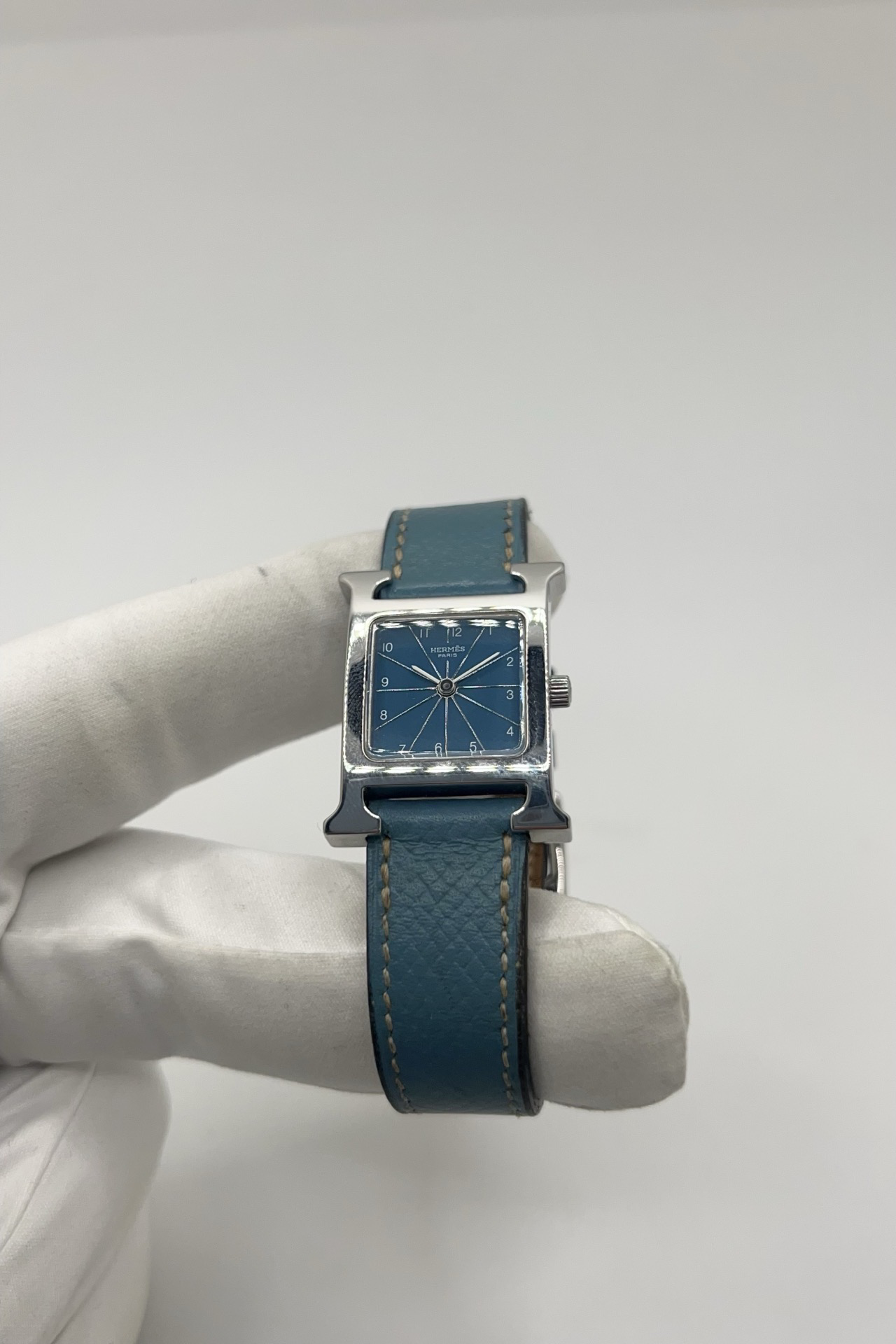Montre Hermès Heure H HH1.210 en acier avec cadran bleu à chiffres arabes et bracelet cuir Hermès bleu d’origine. Cette montre Hermès femme quartz au design iconique en forme de H incarne l’élégance parisienne et le luxe discret. Modèle Hermès Heure H acier de 21 x 30 mm avec verre saphir, boucle ardillon acier et mouvement quartz fiable. Montre de luxe féminine chic et intemporelle, révisée et livrée avec certificat d’authenticité.