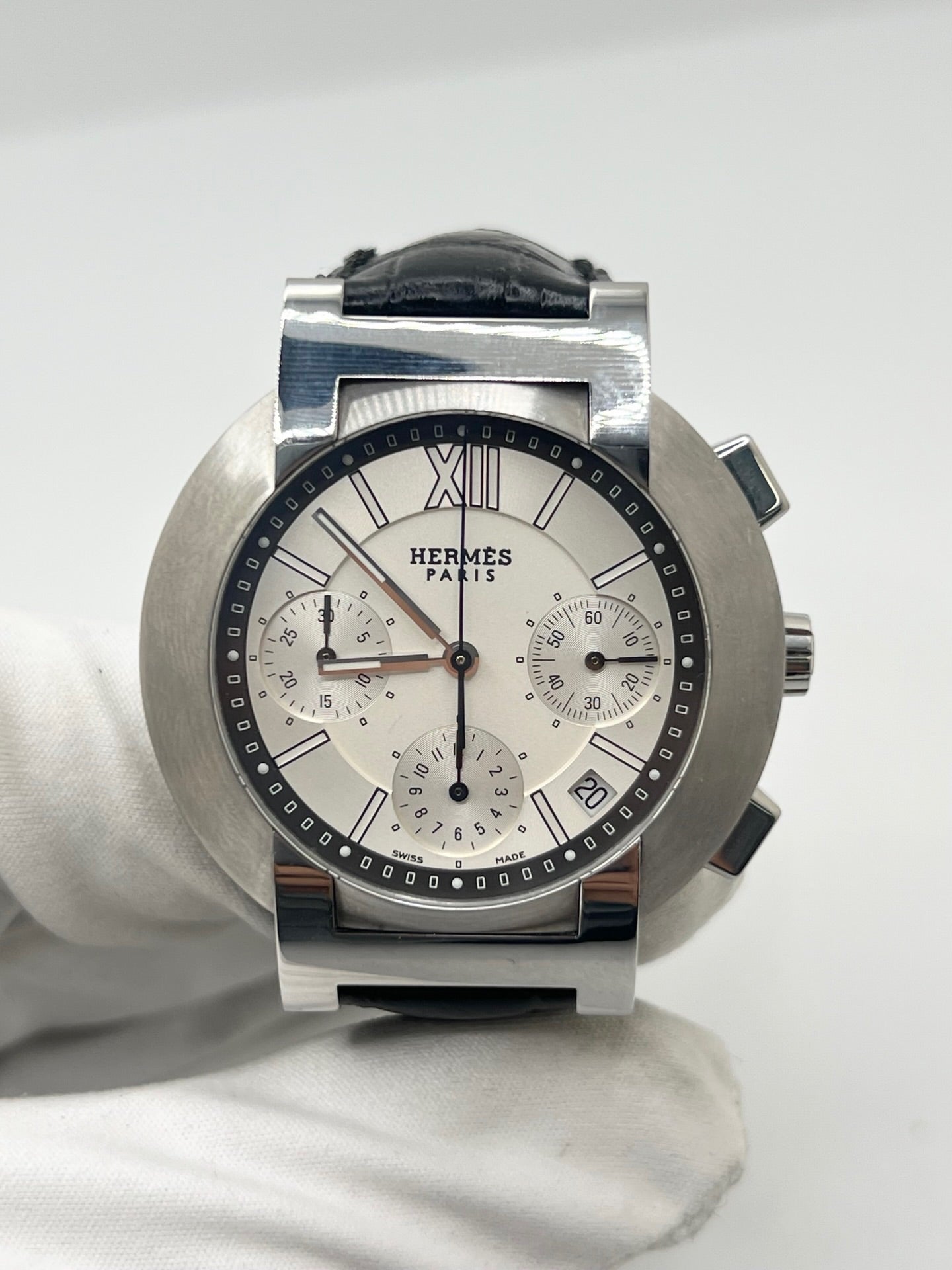 Montre Hermès Nomade Chronograph en acier avec boîtier de 39 mm et cadran blanc à index bâtons. Ce chronographe à mouvement quartz est équipé d’un verre saphir, d’un affichage de la date et d’un bracelet en cuir de crocodile gris avec boucle déployante en acier. Son design élégant et sportif reflète le savoir-faire horloger de la maison Hermès. Modèle unisexe d’occasion en très bon état, alliant confort, précision et raffinement au quotidien.
