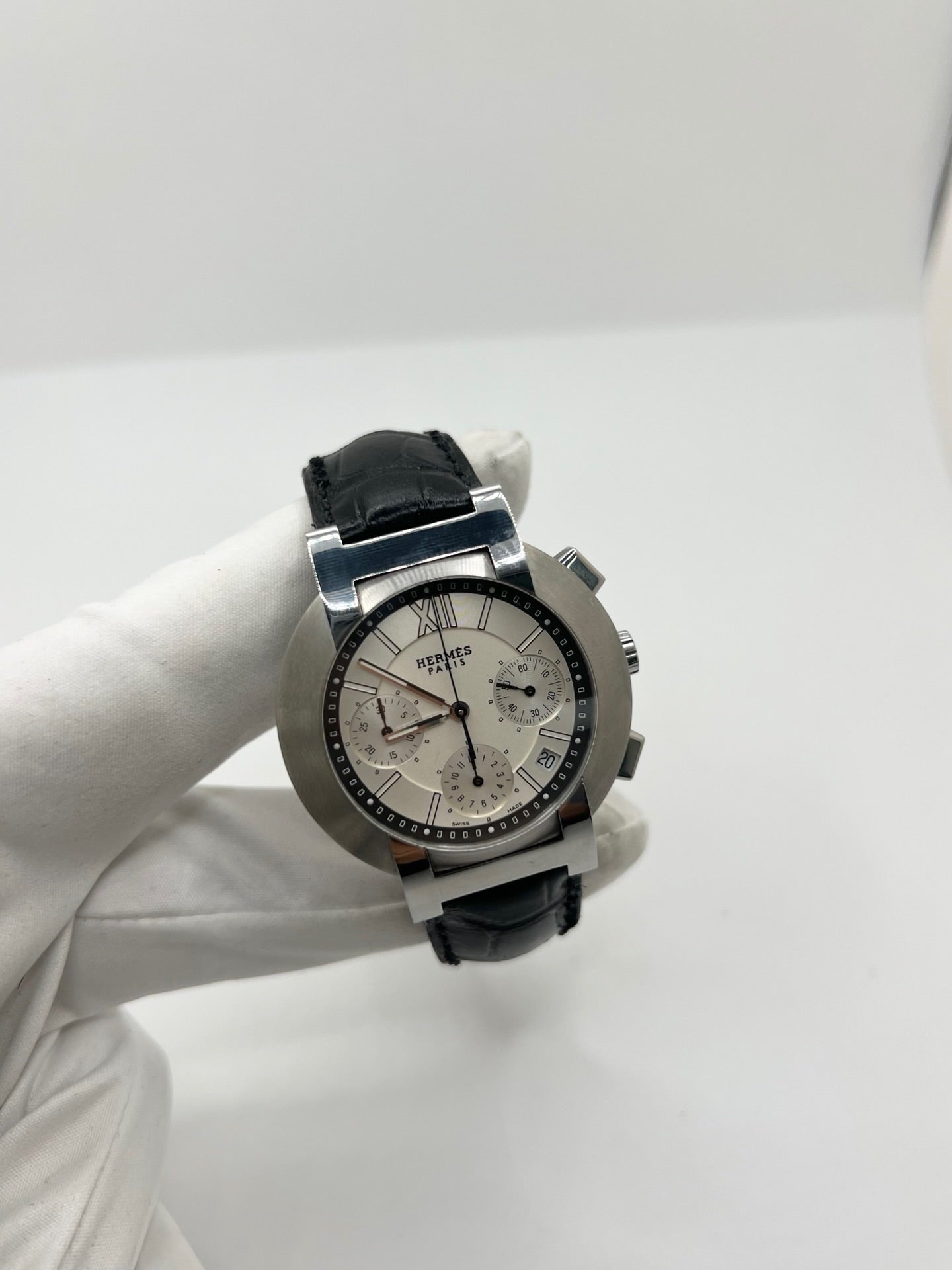 Montre Hermès Nomade Chronograph en acier avec boîtier de 39 mm et cadran blanc à index bâtons. Ce chronographe à mouvement quartz est équipé d’un verre saphir, d’un affichage de la date et d’un bracelet en cuir de crocodile gris avec boucle déployante en acier. Son design élégant et sportif reflète le savoir-faire horloger de la maison Hermès. Modèle unisexe d’occasion en très bon état, alliant confort, précision et raffinement au quotidien.
