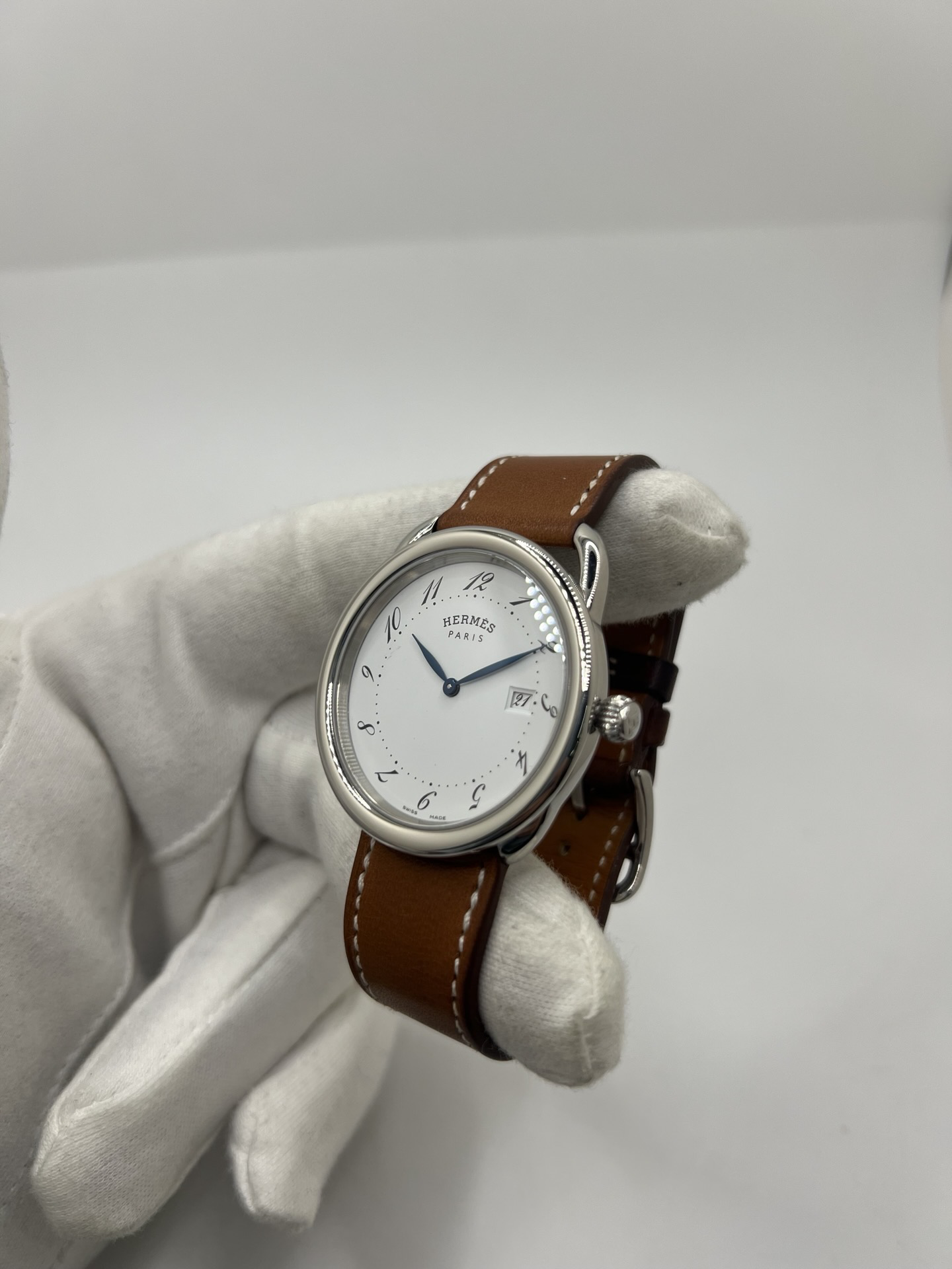 Montre Hermès Arceau Grand Modèle AR5.710 de 2014 en acier 38 mm avec mouvement quartz, cadran blanc à chiffres arabes et bracelet cuir brun d’origine. Cette montre de luxe Hermès Full Set avec boîte et papiers possède un verre saphir, une boucle ardillon acier et le design emblématique Arceau inspiré de l’univers équestre. Montre vintage Hermès élégante, révisée en 2026 et garantie 1 an.