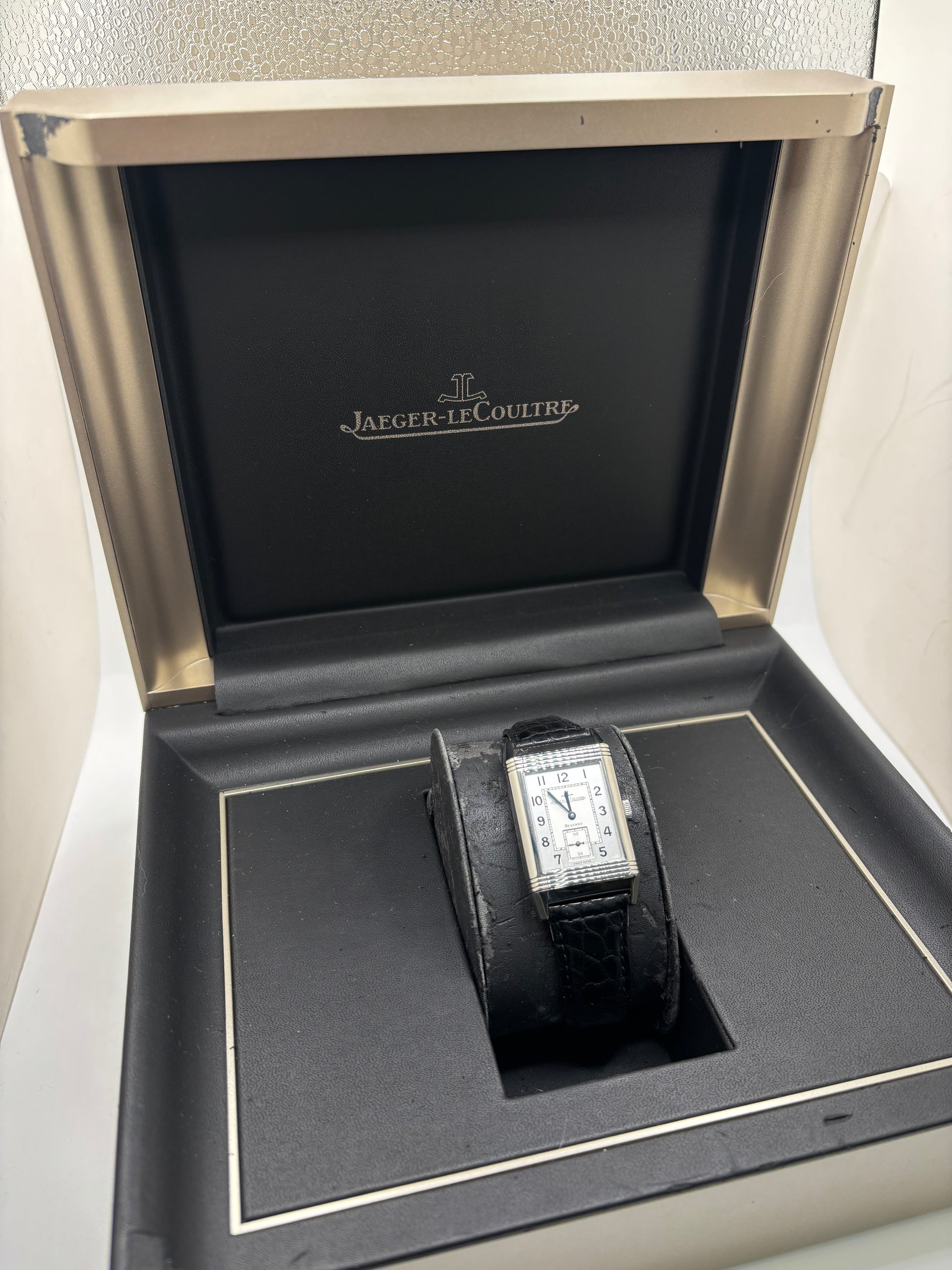 Montre Jaeger-LeCoultre Reverso Grande Taille 270.8.62 en acier, mouvement mécanique à remontage manuel calibre 822. Boîtier rectangulaire 26 x 42 mm, cadran argent à chiffres arabes, petite seconde, verre saphir. Bracelet cuir noir boucle ardillon acier. Modèle 1997 en très bon état, révisé le 4 juin 2026, livré avec coffret et papiers d’origine. Montre de luxe suisse emblématique, design Art déco, style vintage élégant. pièce horlogère iconique.
